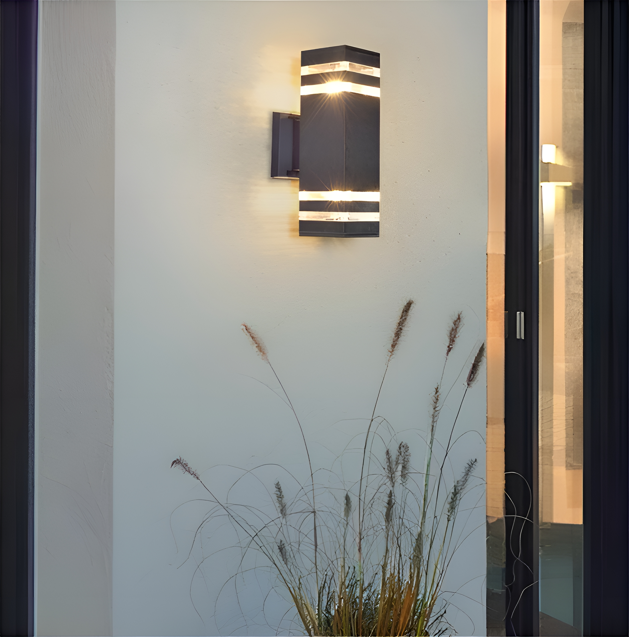 Außenwandleuchte an einer weißen Wand. Das Licht ist schwarz mit horizontalen Lichtstreifen. Gras davor.