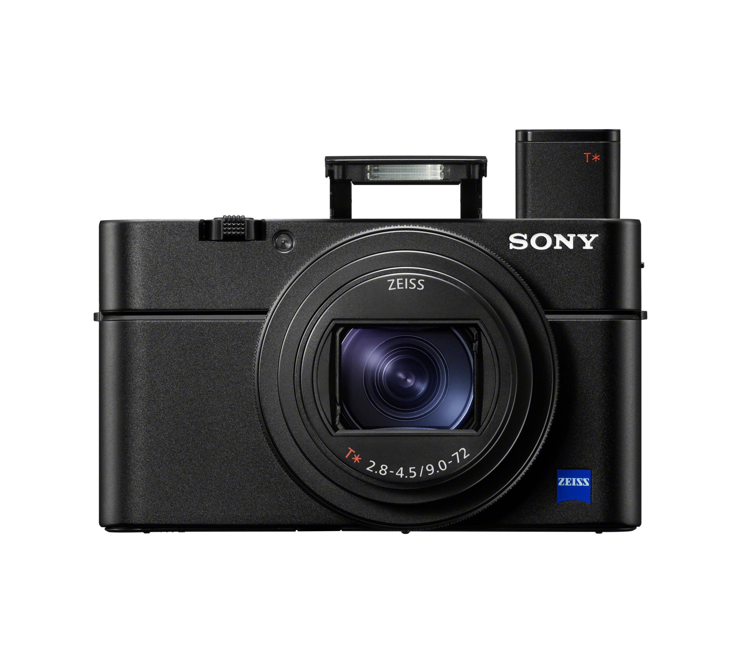 Una cámara Sony negra con una lente plateada y la palabra ZEISS en la lente. La cámara está sobre una superficie blanca.