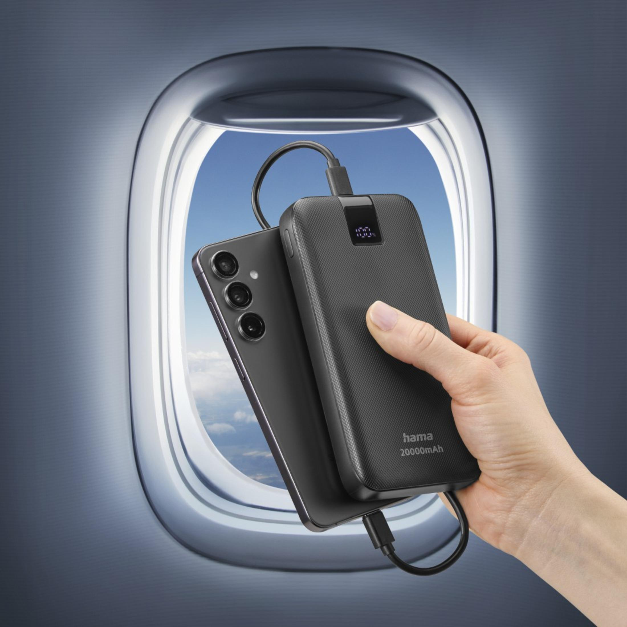 Mano che tiene un power bank nero vicino a un telefono, vista attraverso un finestrino dell'aereo.