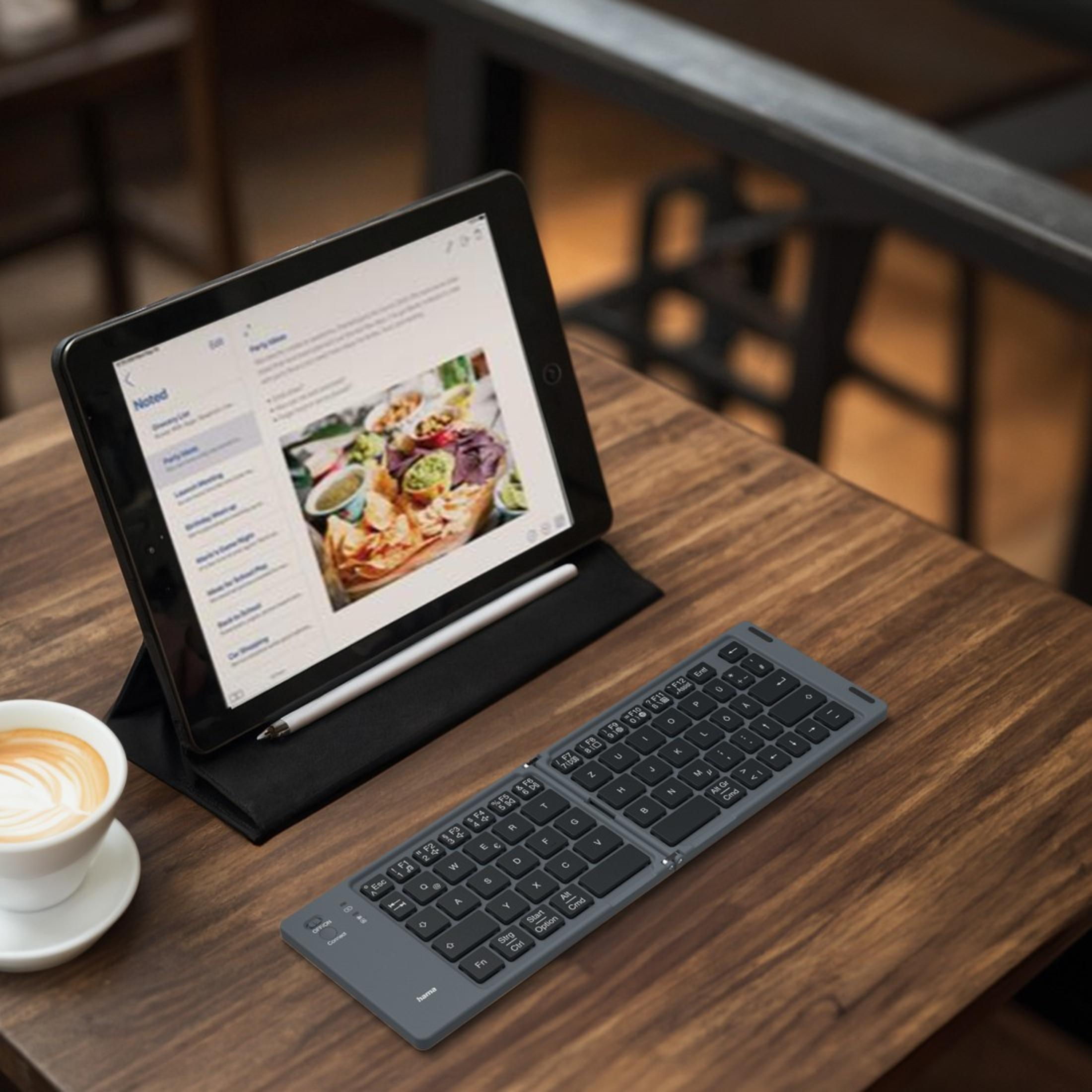 Un tablet su un tavolo di legno con una tastiera e una tazza di caffè.