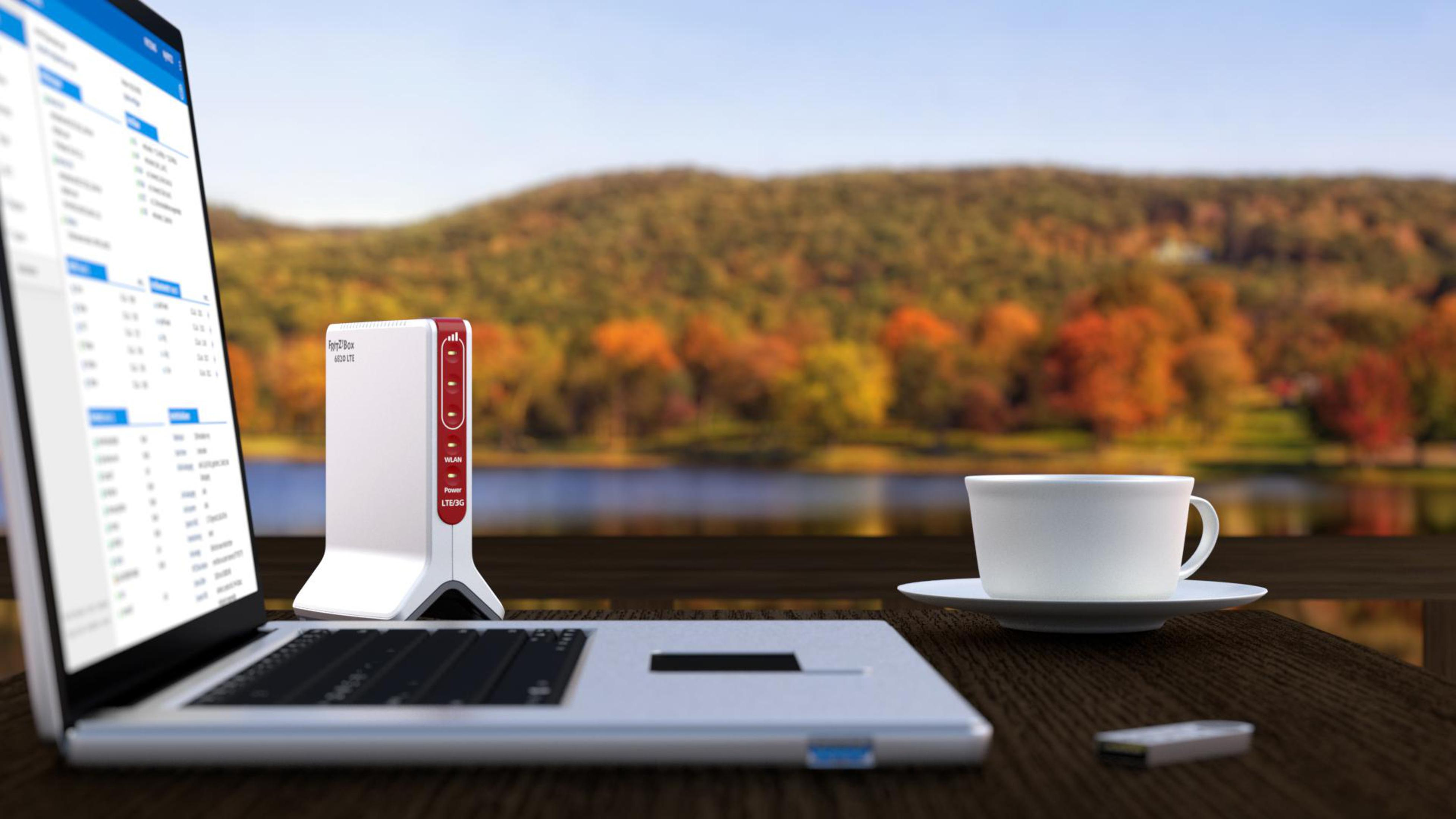 Ein Laptop und Router-Setup mit einer malerischen Kulisse aus See und Bäumen in Herbstfarben.