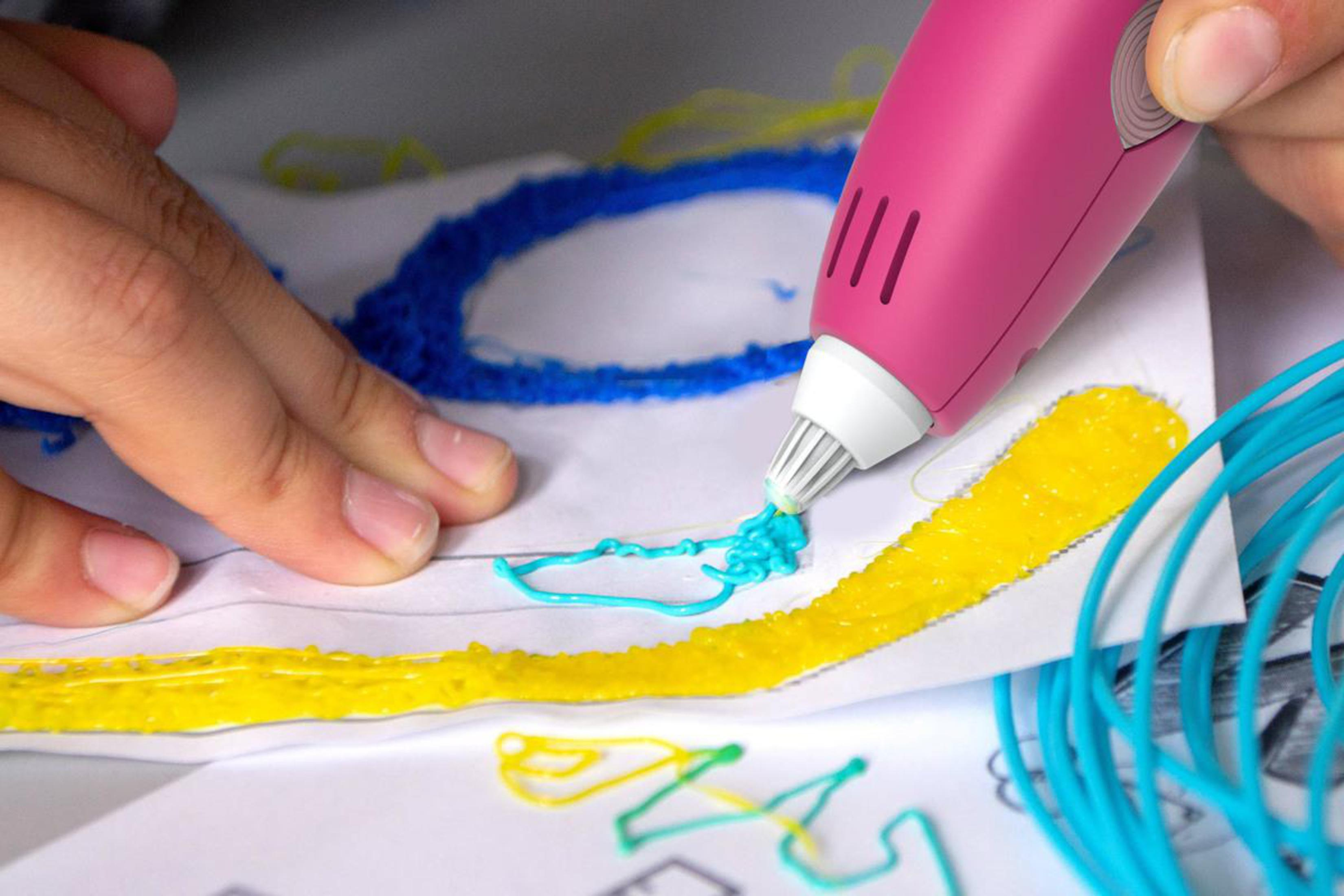 Eine Person, die einen pinkfarbenen 3D-Stift zum Zeichnen auf Papier verwendet. Gelbe und blaue Linien sind sichtbar.