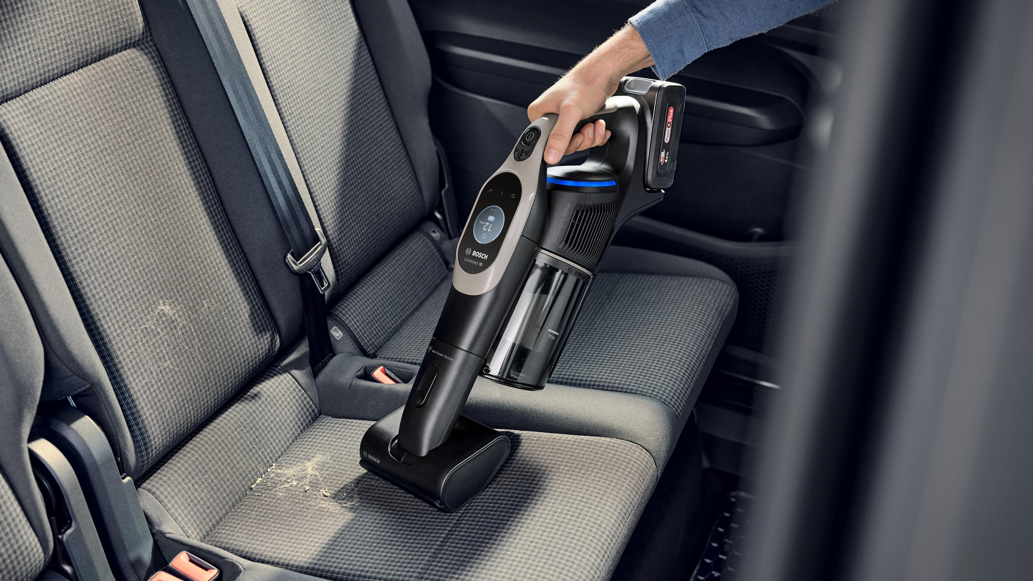 Una persona aspirando un asiento de coche con una aspiradora de mano.