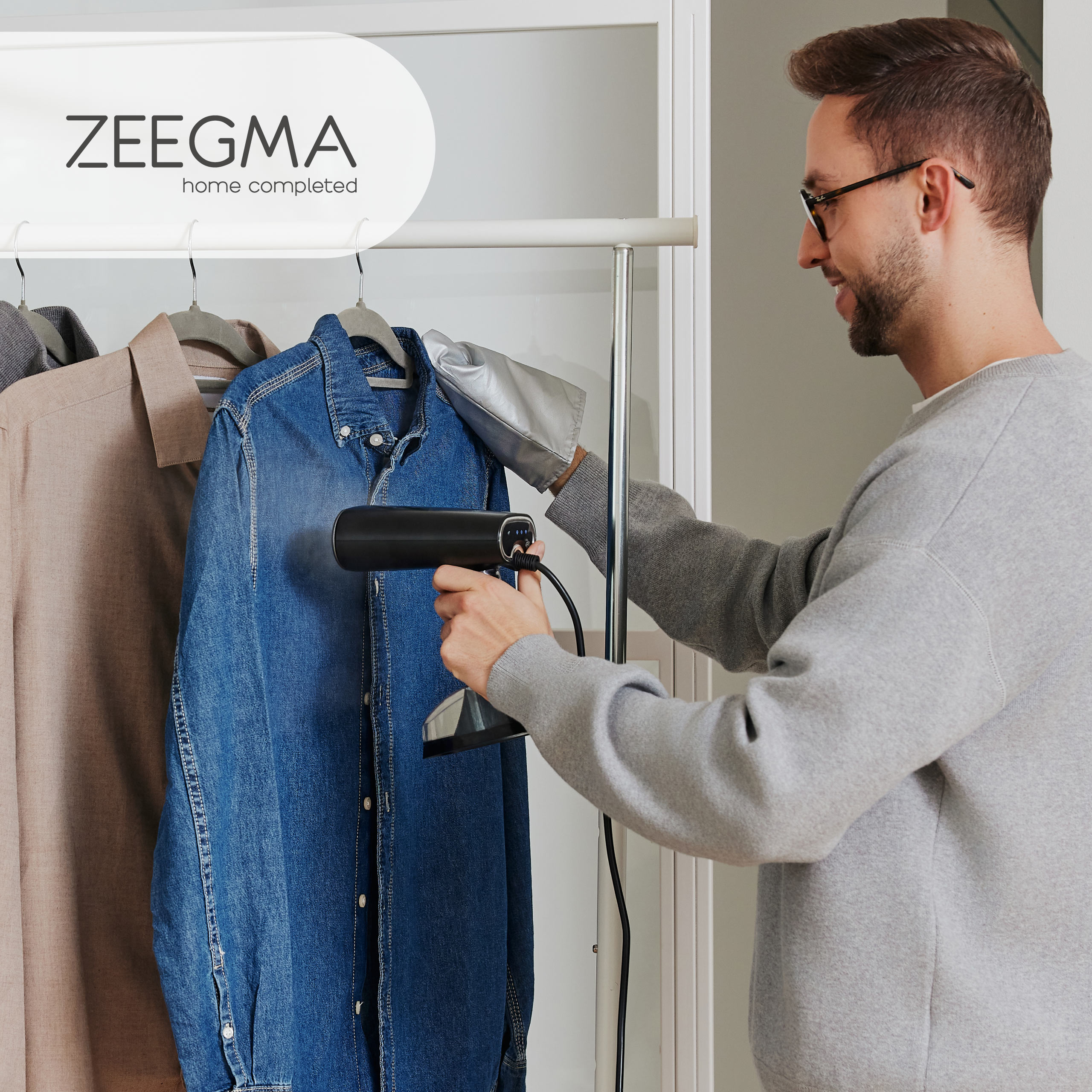 Mann, der einen Kleiderdampfer an einem auf einem Gestell hängenden Jeanshemd verwendet.