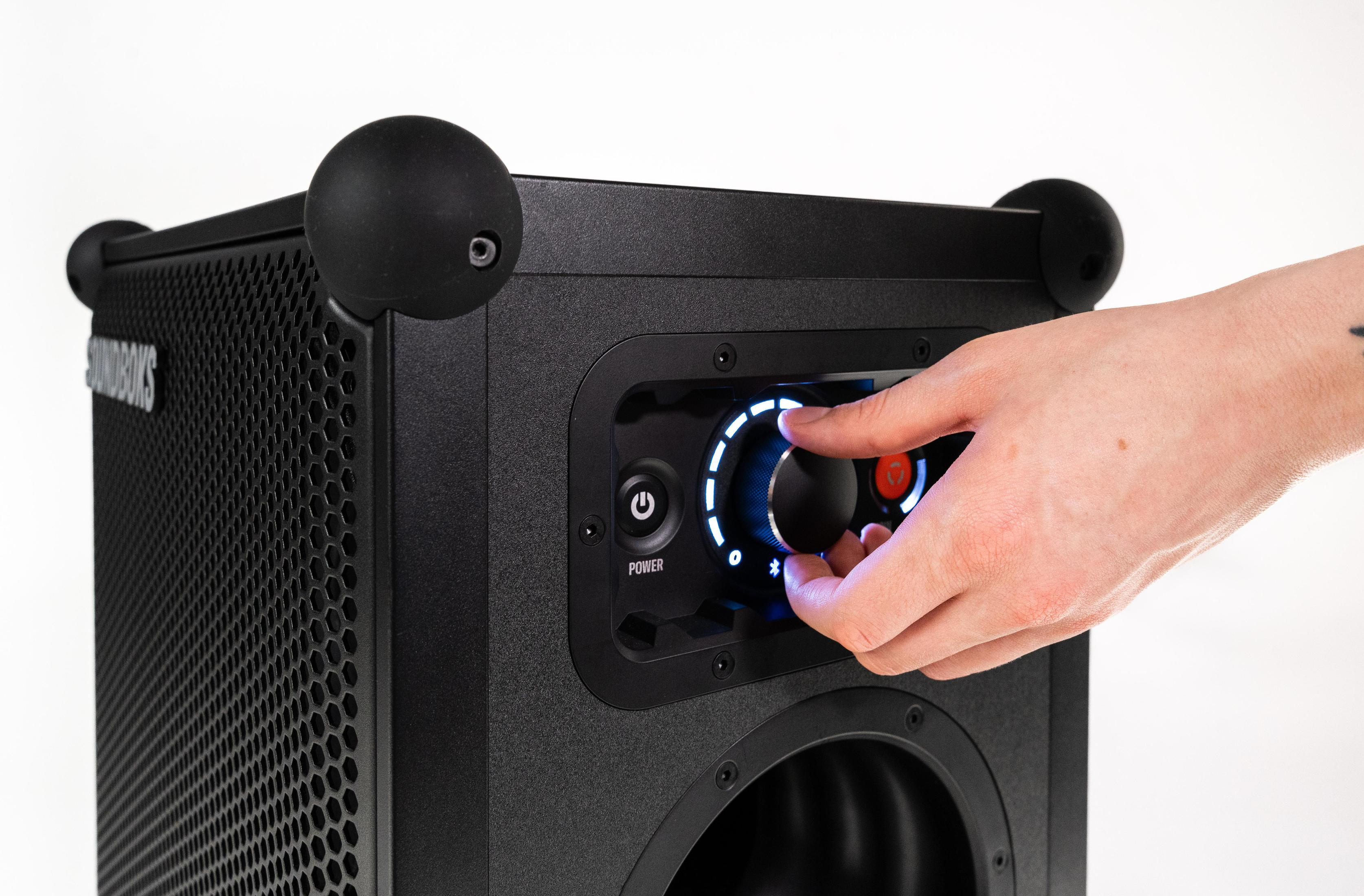Person stellt Lautstärkeregler an schwarzer Soundbox ein. Weißer Hintergrund.