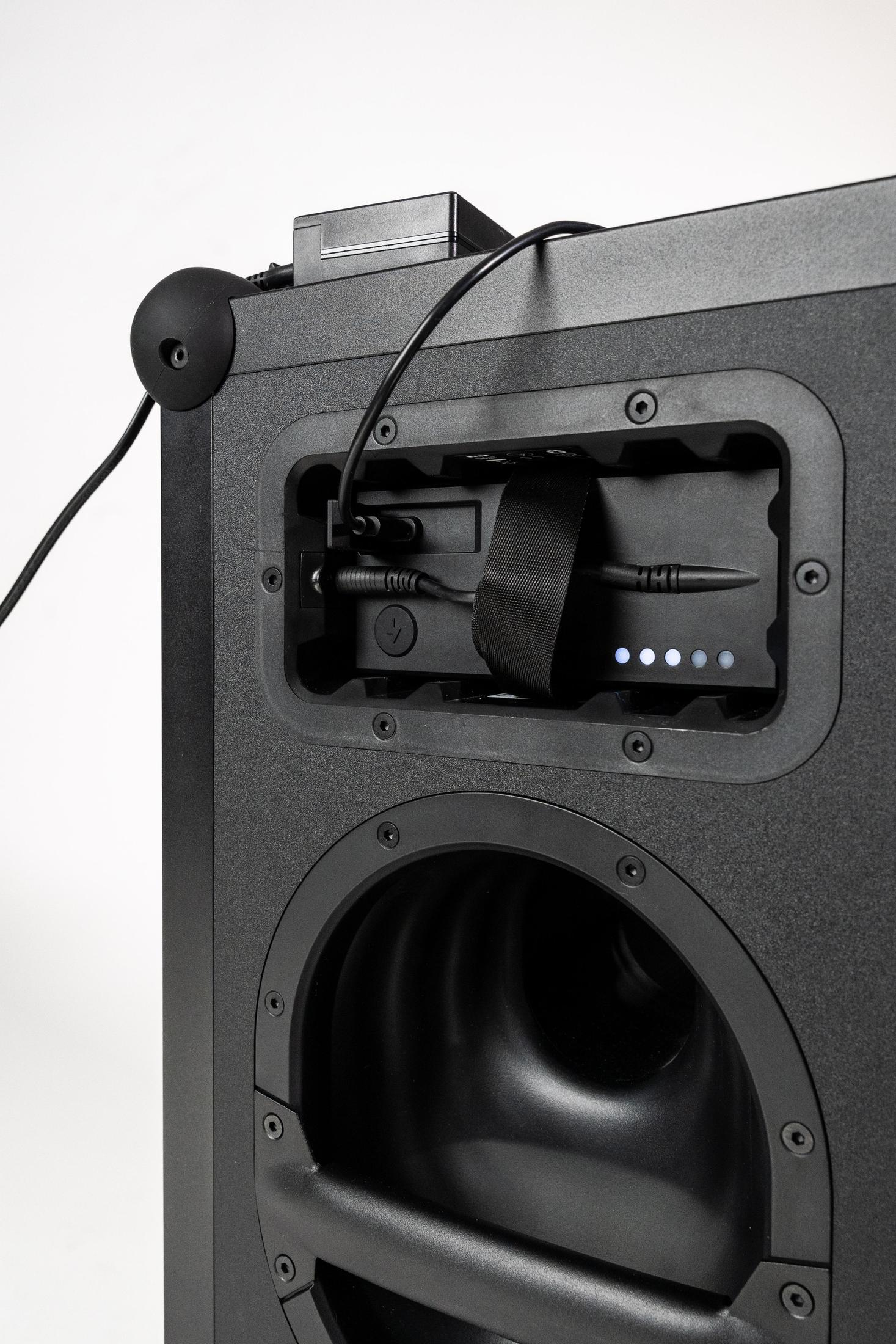 Rückansicht eines schwarzen Lautsprechers mit Batteriefach. Ladekabel und Batteriestandsanzeige.