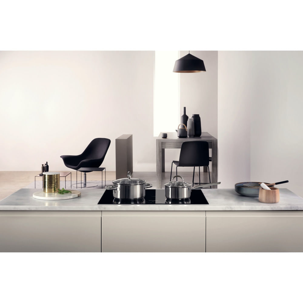 Scena kuchenna z blatem i płytą grzejną. Na blacie stoją garnki, patelnie i elementy dekoracyjne.