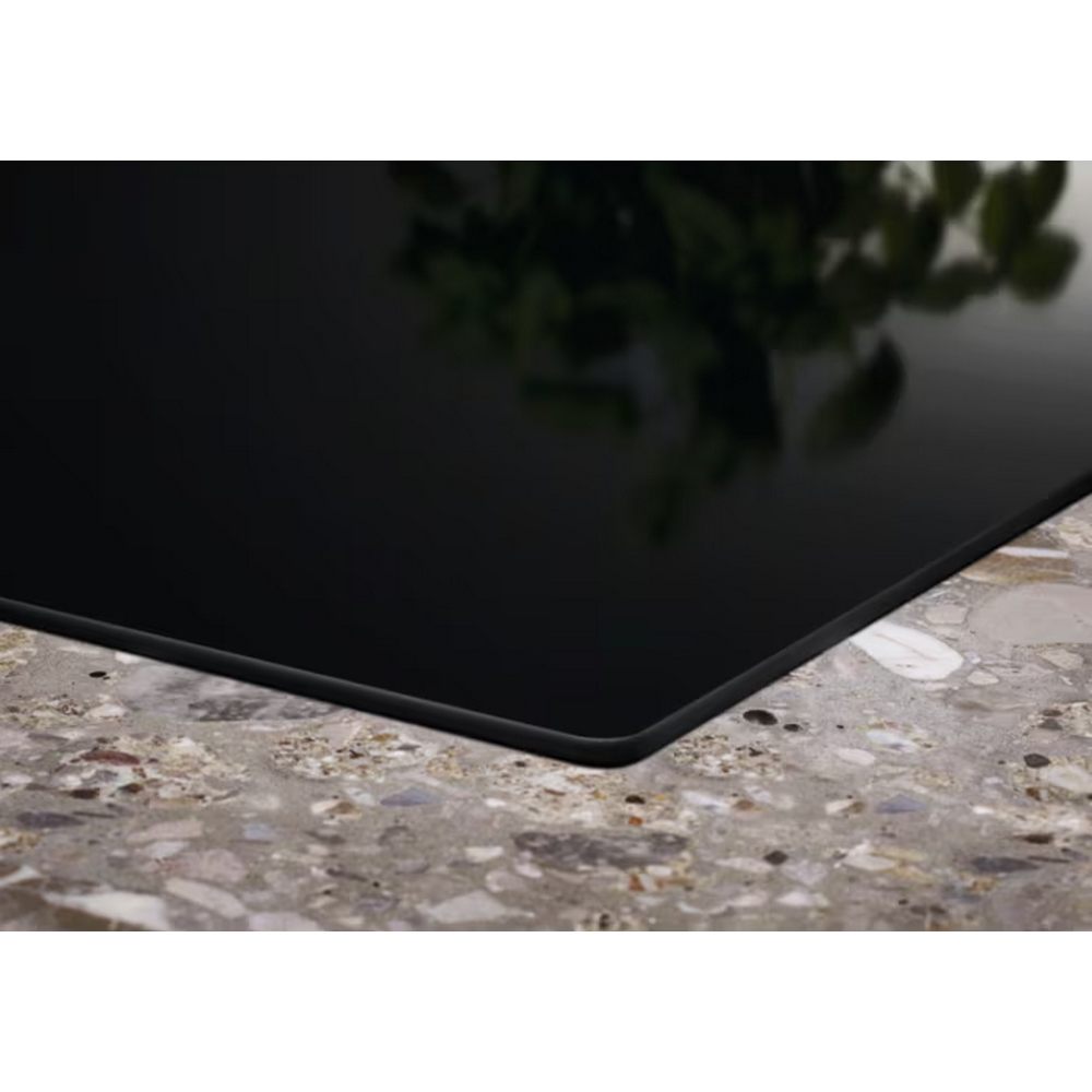 Czarna szklana płyta grzewcza z rozmytym tłem zieleni. Powierzchnia odbija światło.