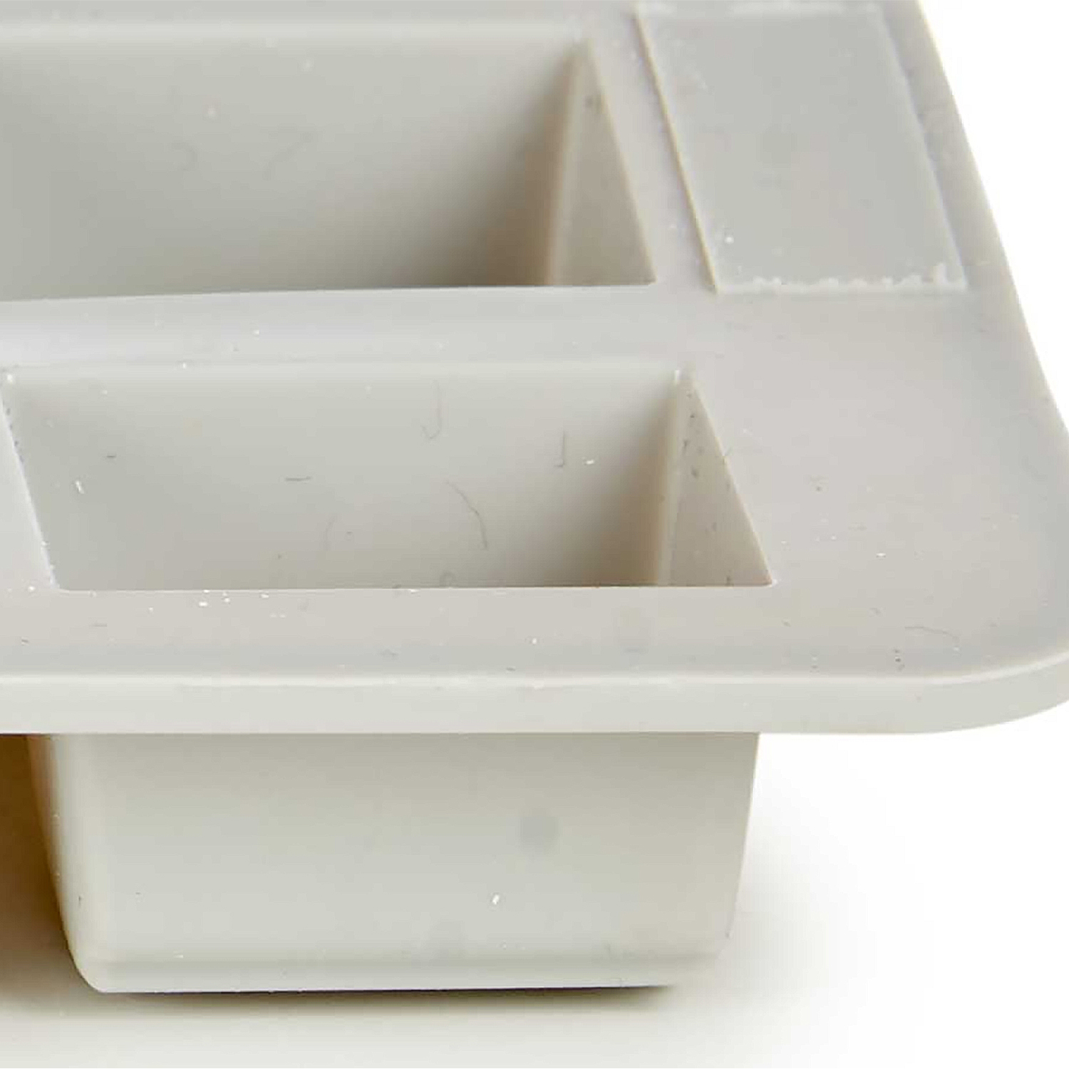 Uno stampo in silicone rettangolare grigio chiaro con scomparti rettangolari. Sfondo bianco.