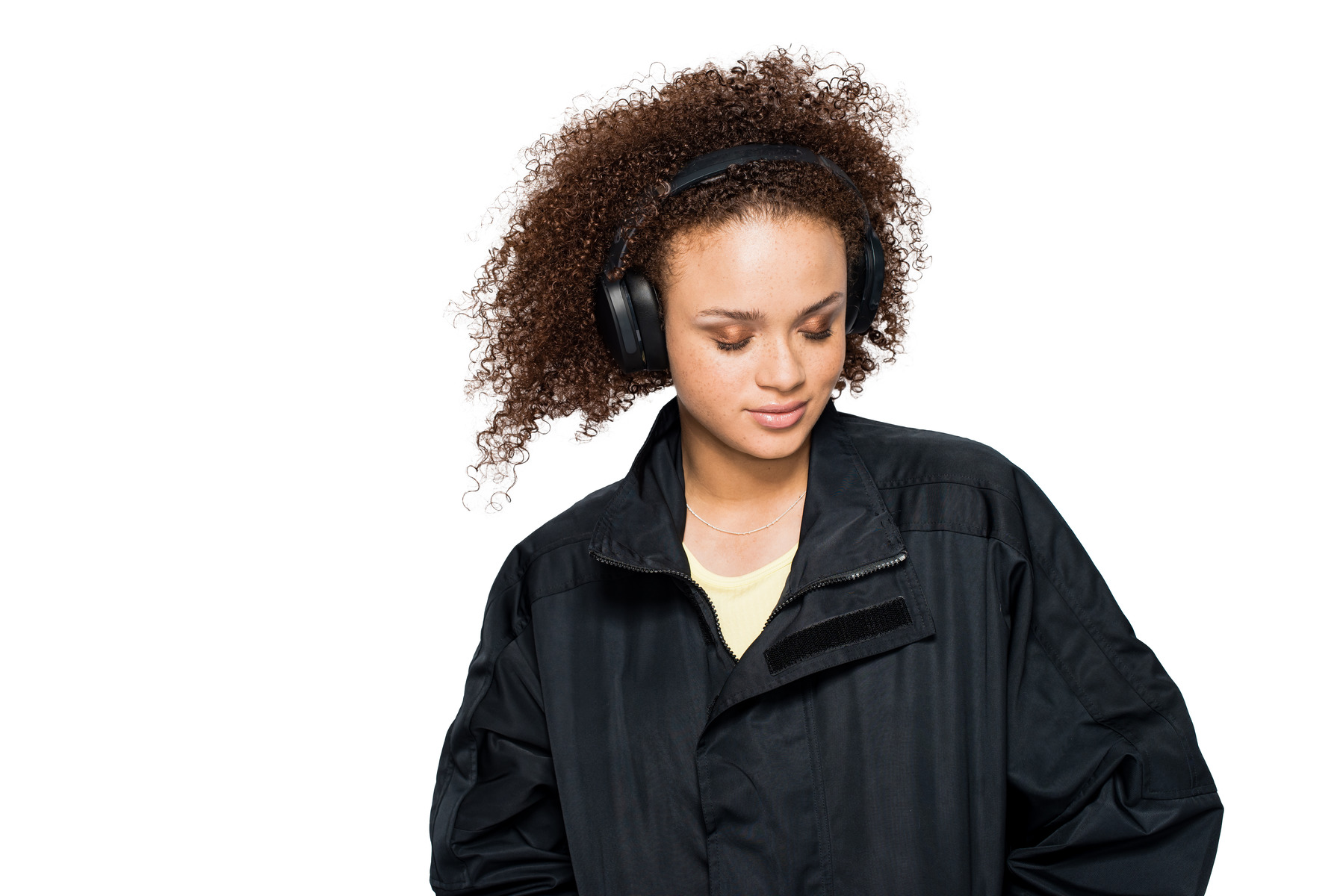 Mujer con auriculares negros y chaqueta negra, fondo blanco.