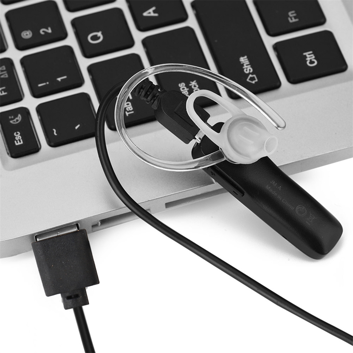 Ein schwarzer Ohrhörer mit einem USB-Kabel, das an einen Laptop angeschlossen ist. Der Ohrhörer befindet sich auf einer Laptop-Tastatur.