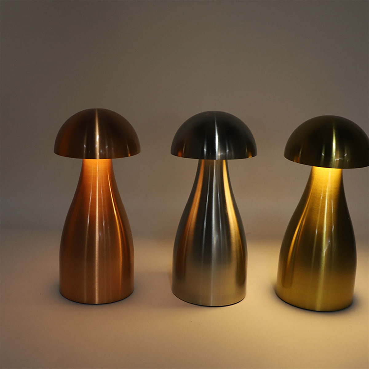 Drei pilzförmige Lampen. Jede hat eine andere metallische Farbe: Bronze, Silber und Gold.