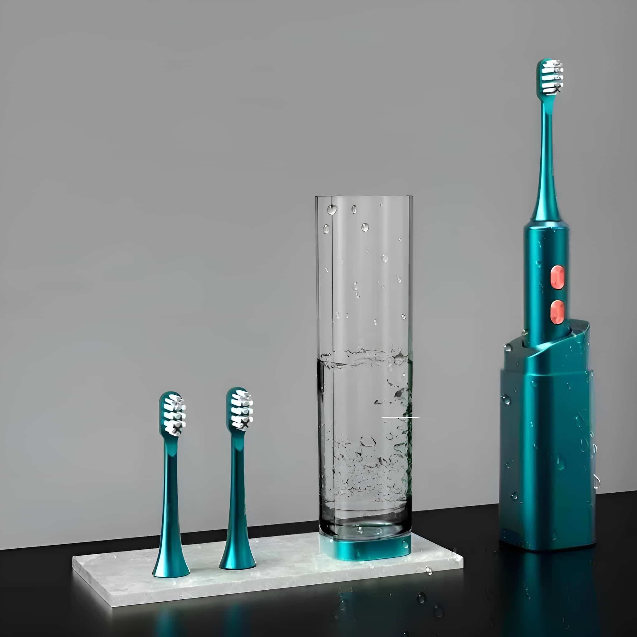 Eine elektrische Zahnbürste, zwei Bürstenköpfe und ein Glas Wasser auf grauer Oberfläche.