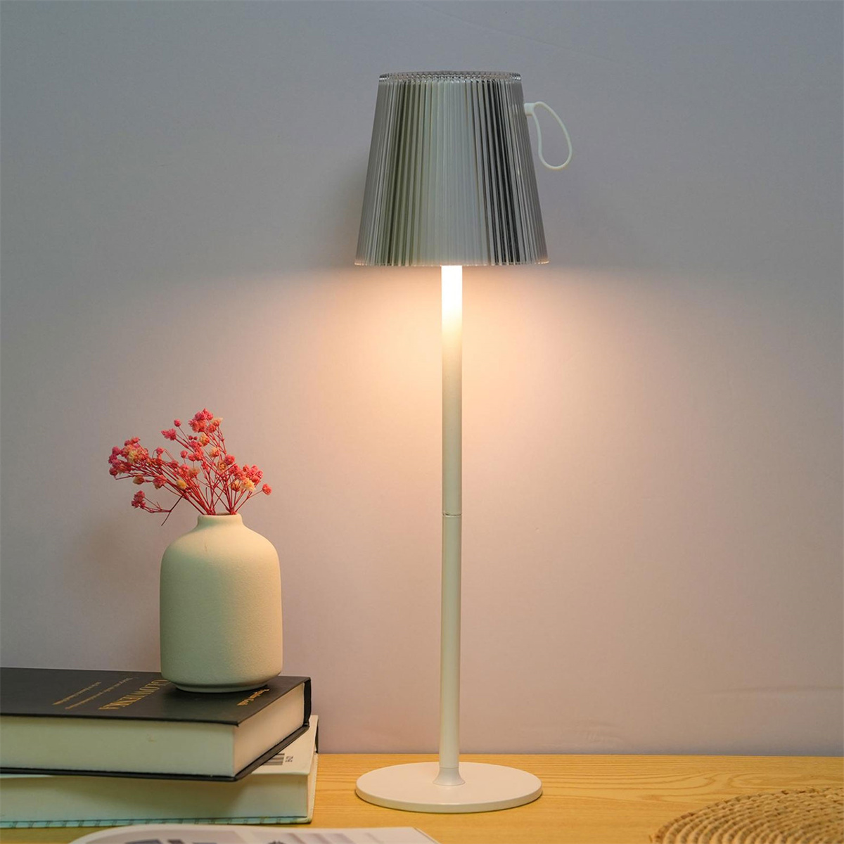Eine weiße Lampe mit transparentem Schirm, neben einer Vase mit Blumen.