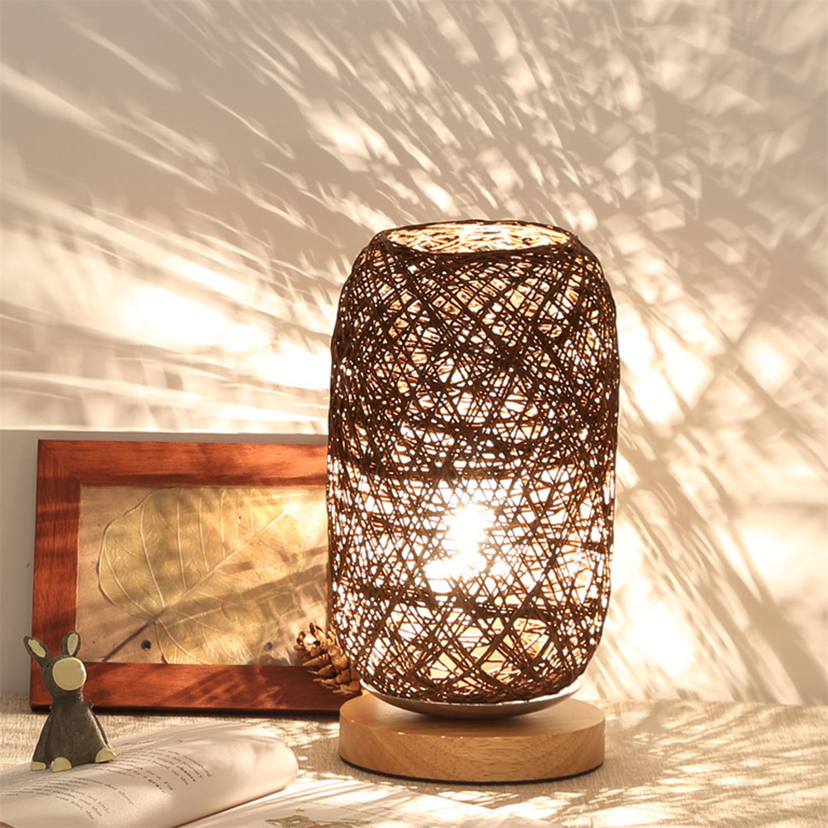 Dekorative gewebte Lampe mit Holzsockel, auf einem Tisch mit Buch und Deko.