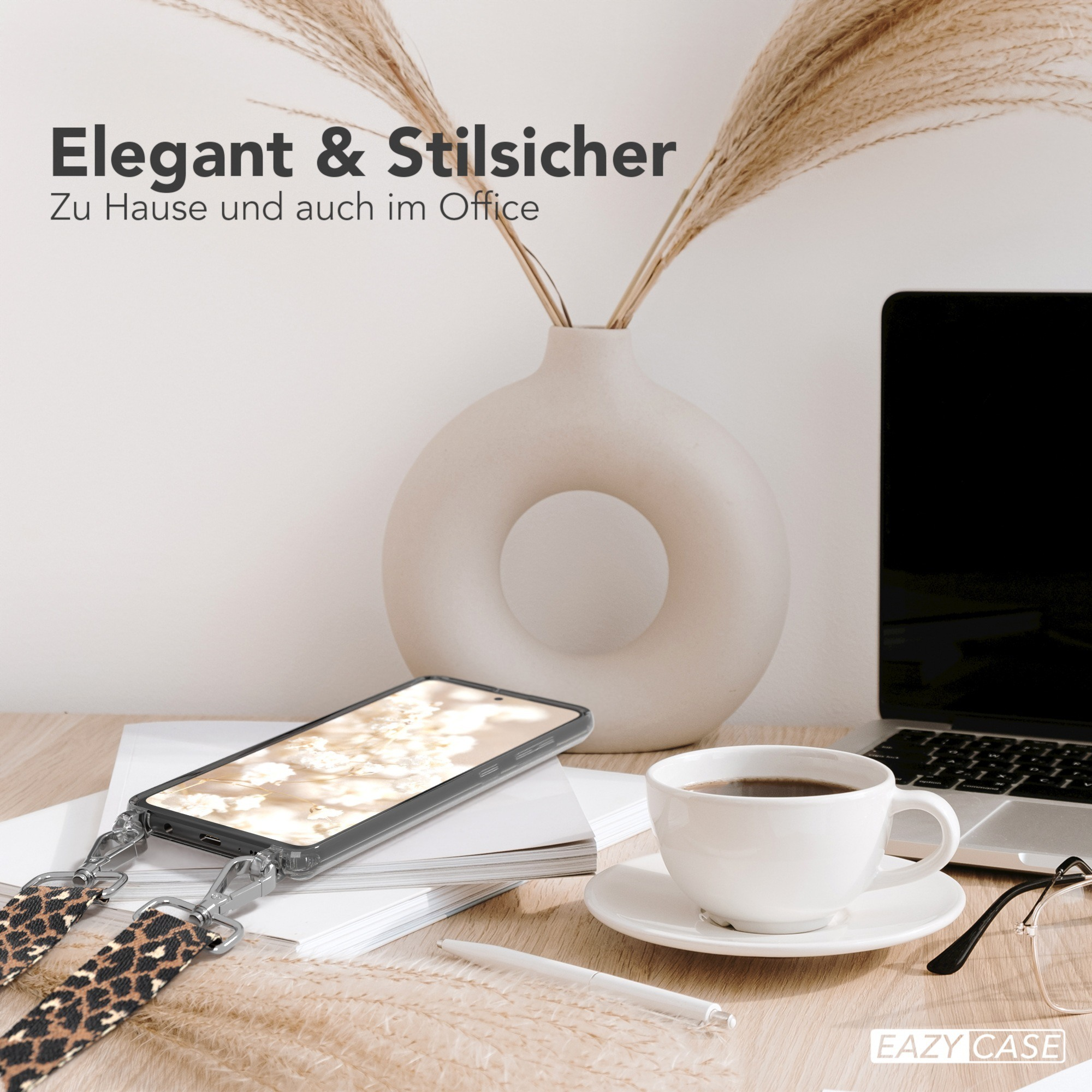 Schreibtisch mit Handyhülle und Kaffeetasse. Ein Laptop, Stift, Brille und Blumen vervollständigen die Szene.