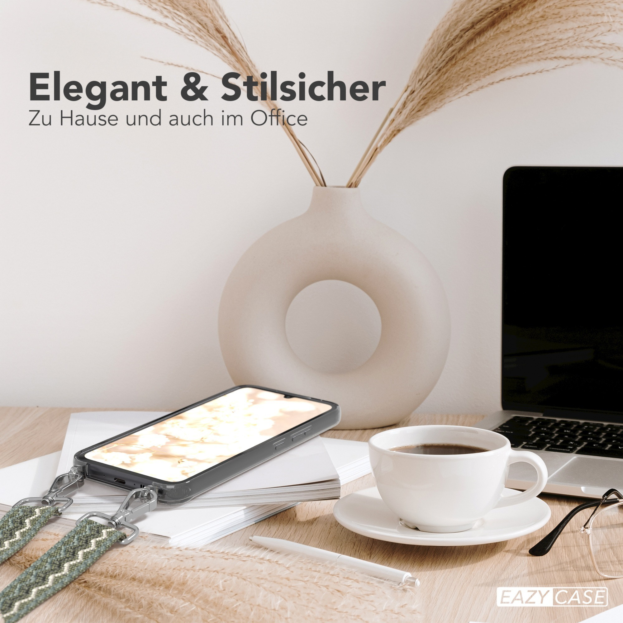 Ein Telefon in einer Hülle mit Riemen, eine Kaffeetasse und ein Laptop auf einem Schreibtisch.