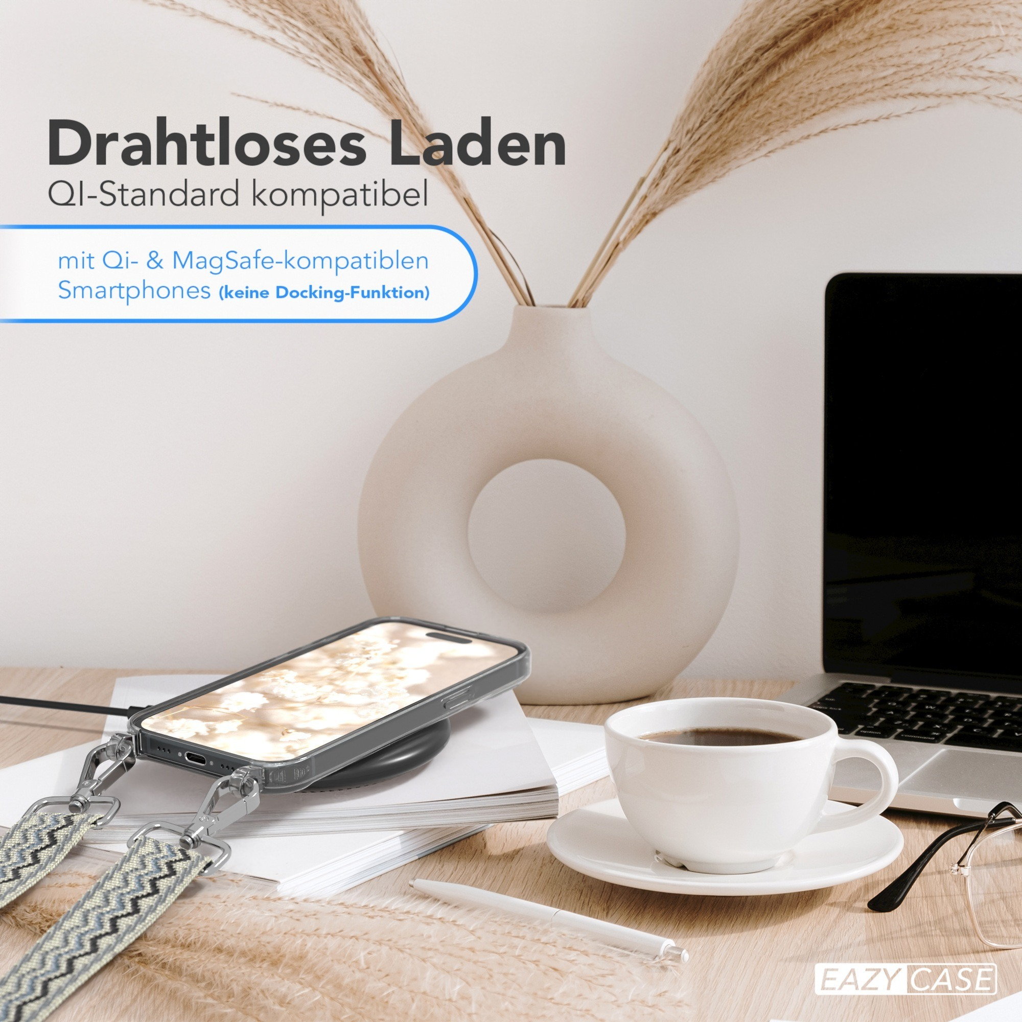 Telefon auf einem kabellosen Ladegerät. Eine Tasse Kaffee, ein Laptop und eine Vase mit Schilf auf einem Schreibtisch.