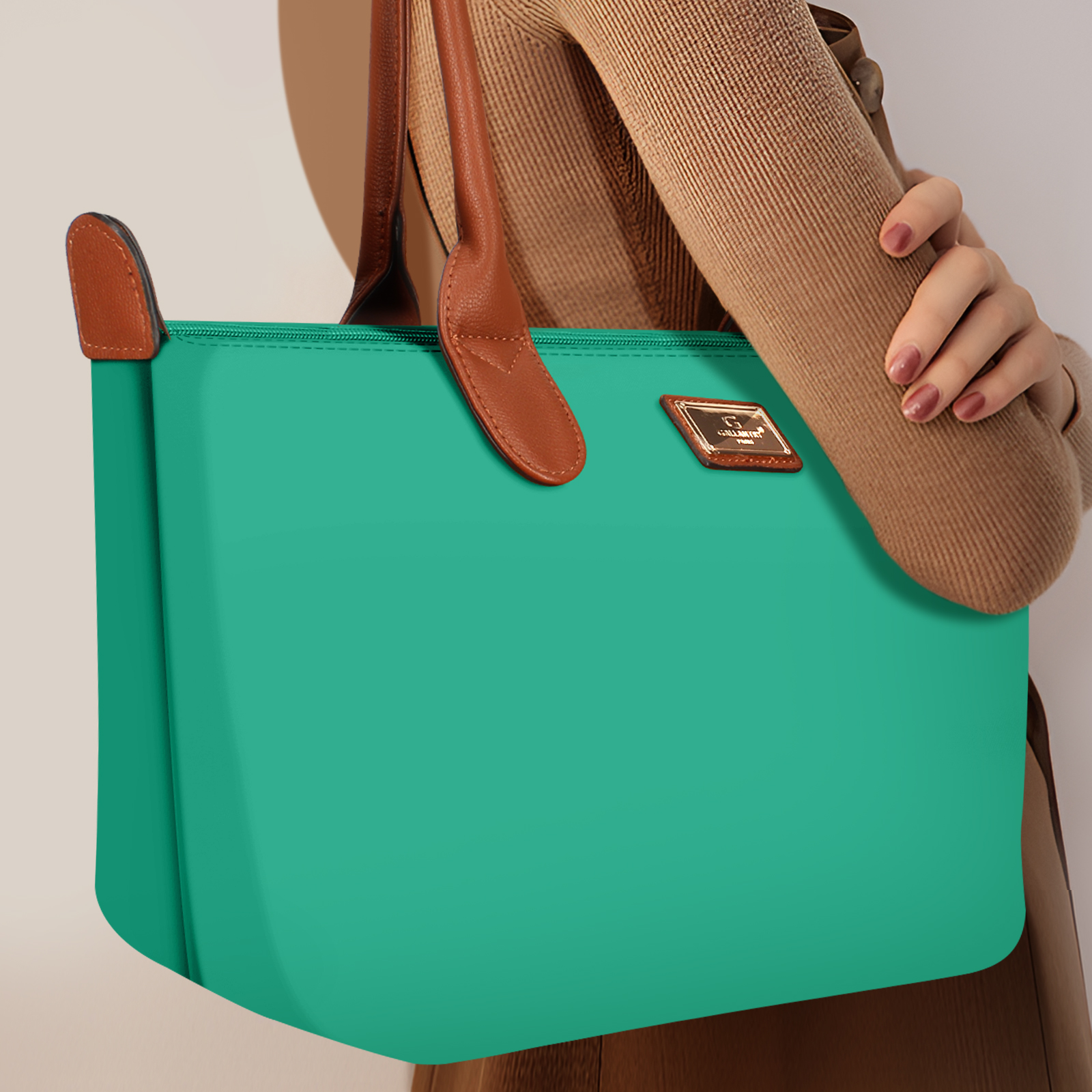 Bolso tote turquesa con asas y detalles marrones. Se adjunta una etiqueta dorada.
