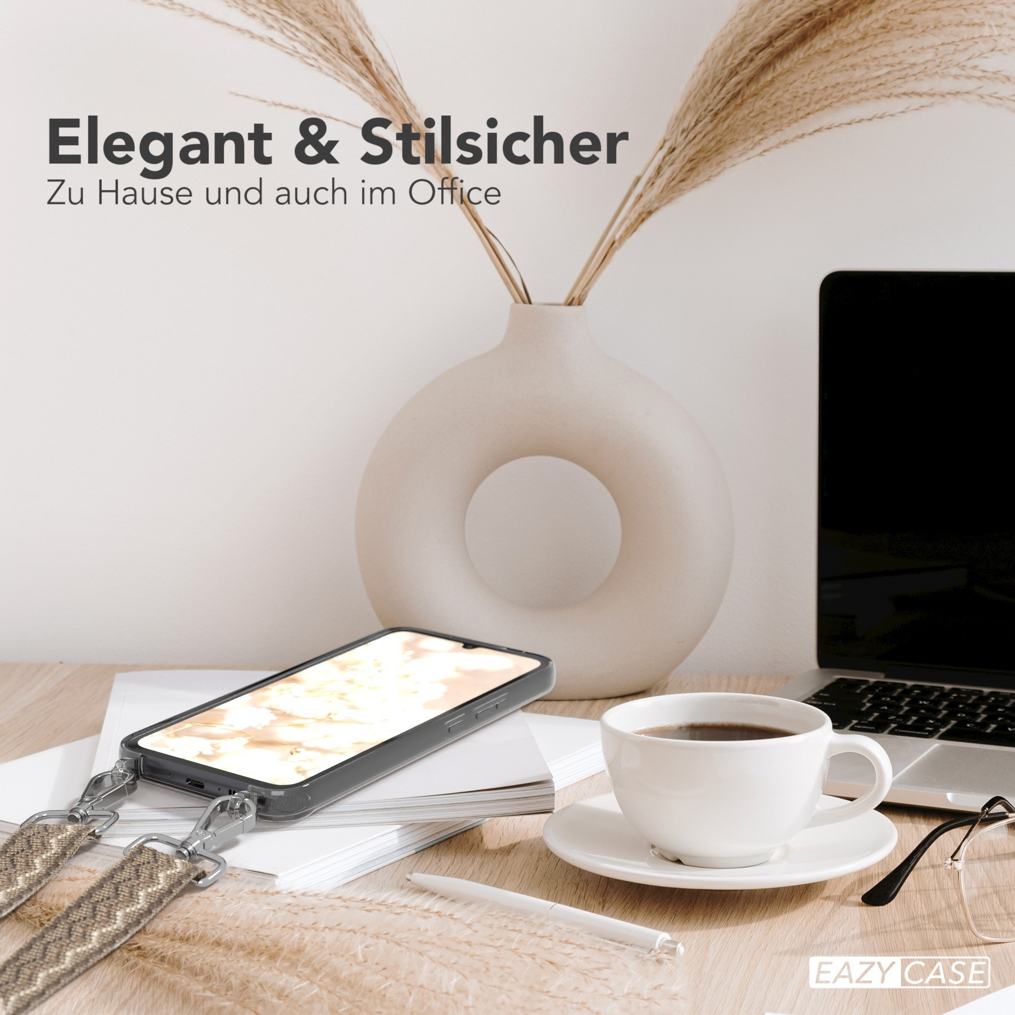 Schreibtisch mit Telefon, Kaffee und Laptop. Eine Vase mit Pampasgras im Hintergrund.