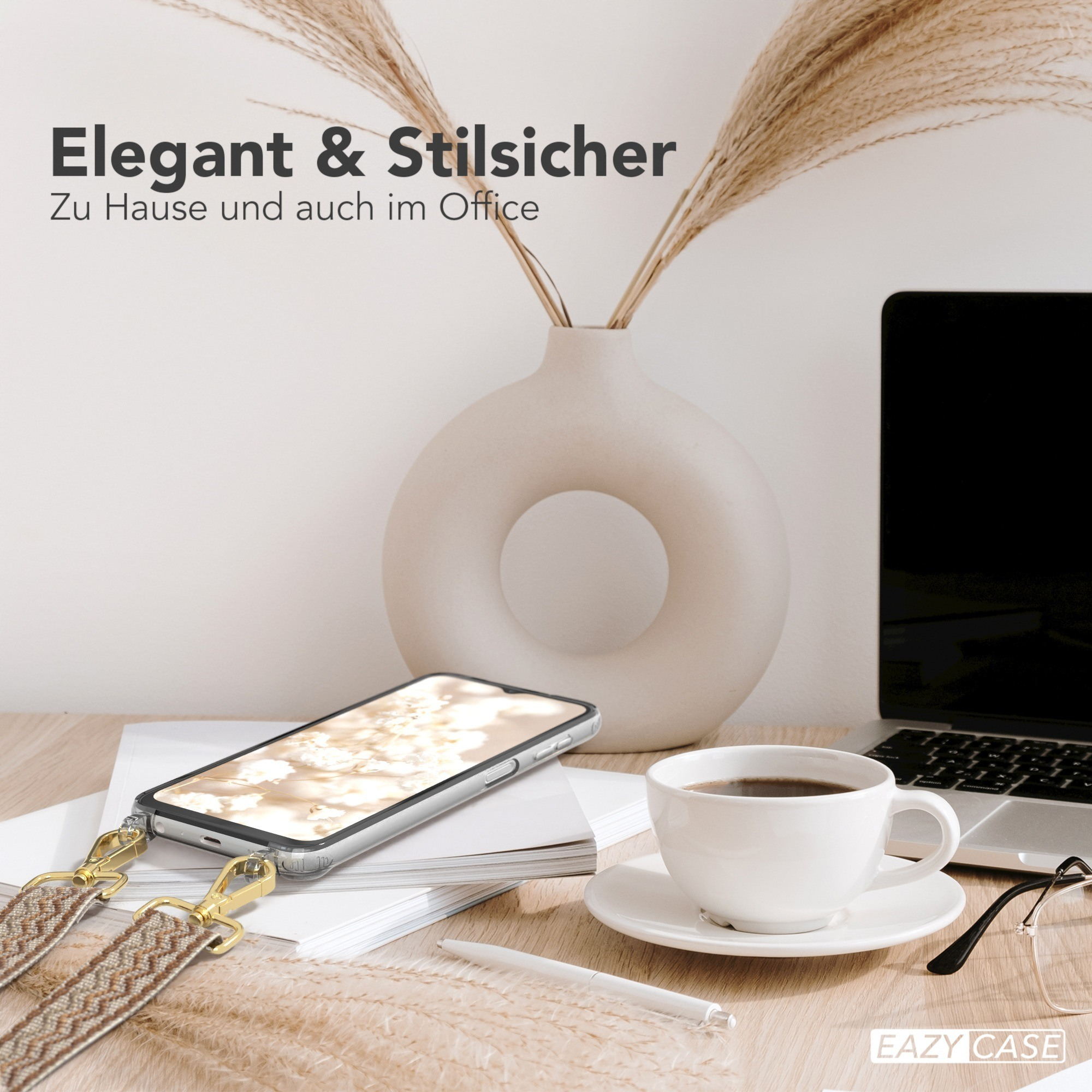 Ein Telefon mit dekorativem Riemen liegt auf einem Schreibtisch mit einem Laptop und einer Kaffeetasse. Dekorative Vase mit Schilf.