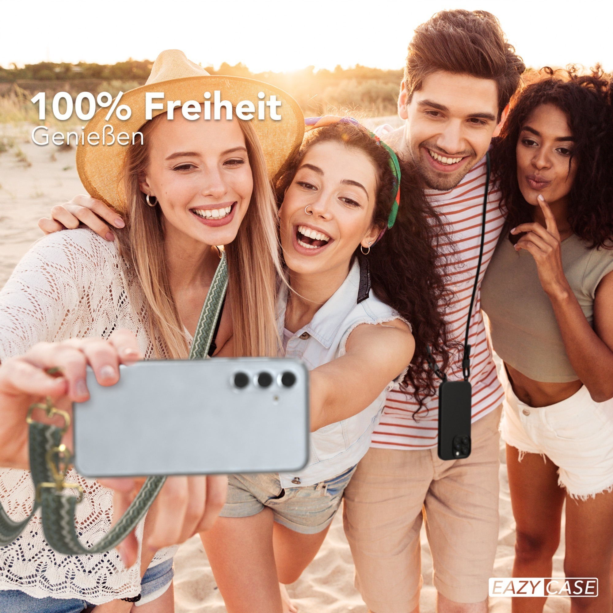 Vier Personen machen ein Selfie am Strand. Einer hält Telefon mit Band, andere lächeln.