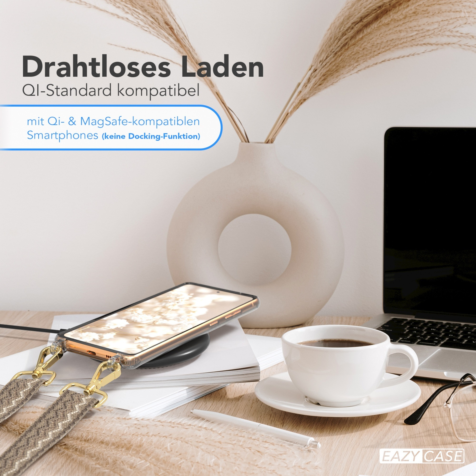 Ein Telefon mit Band liegt auf kabellosem Ladegerät. Kaffeetasse, Laptop und Blumen auf Tisch.