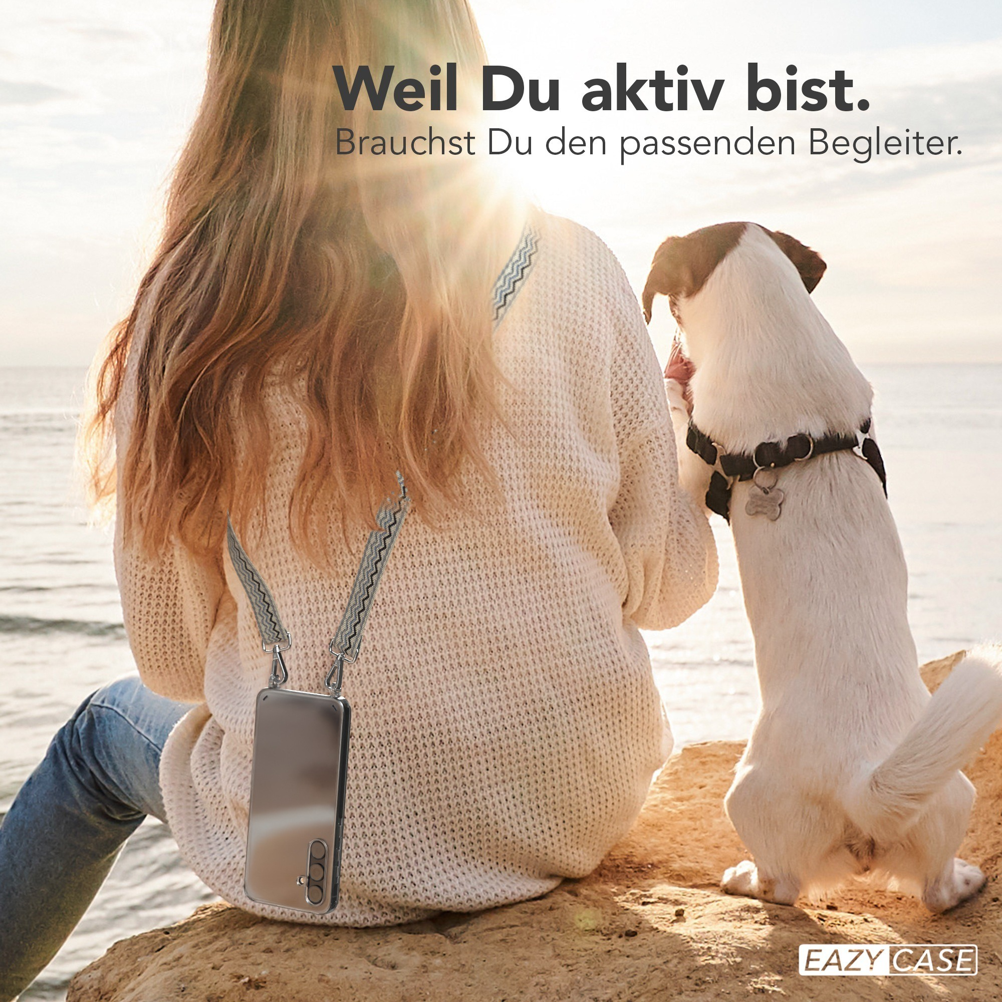 Frau sitzt, Hund springt in der Nähe von Wasser.