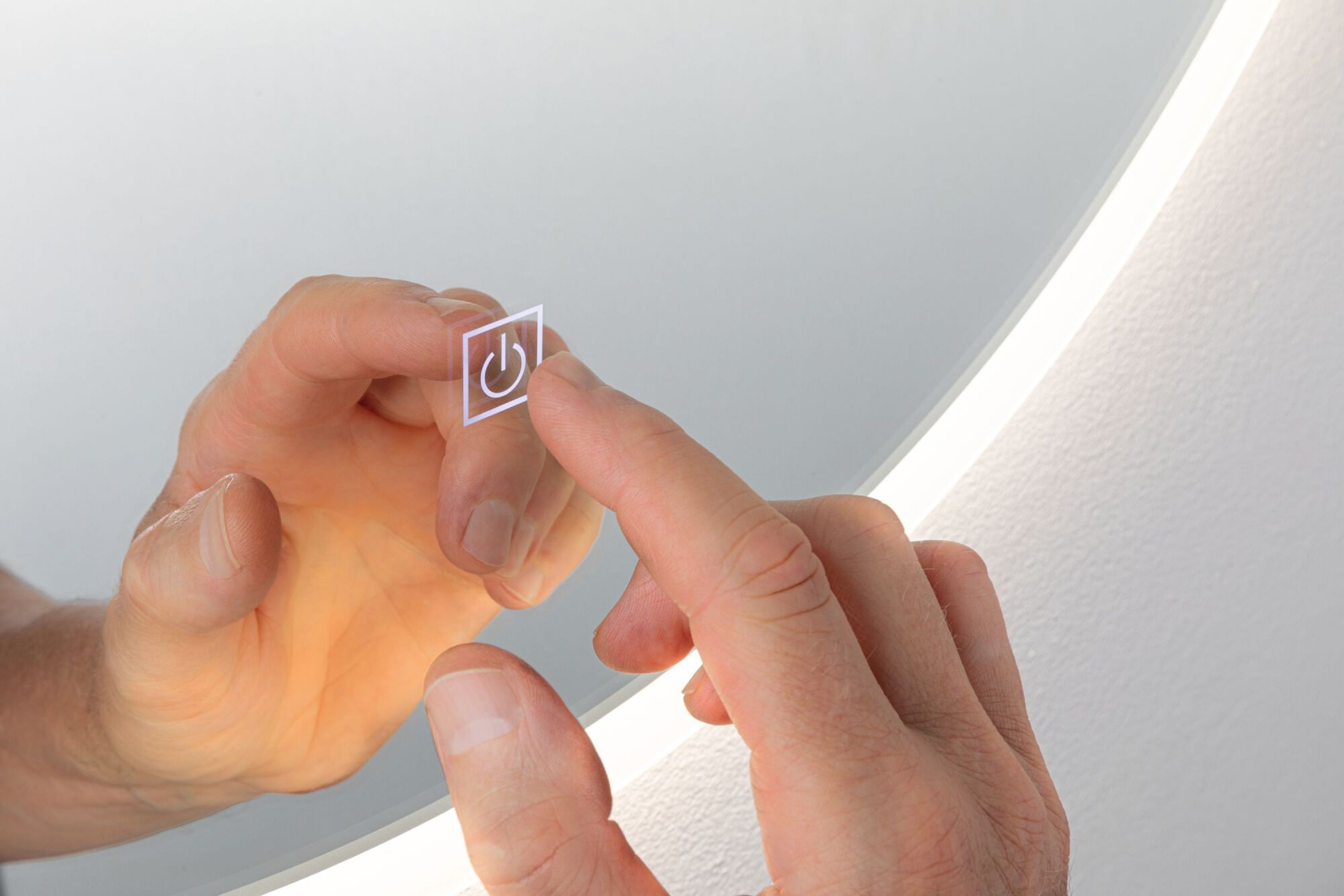 Eine Hand berührt einen Spiegel mit beleuchtetem Einschalt-Symbol.