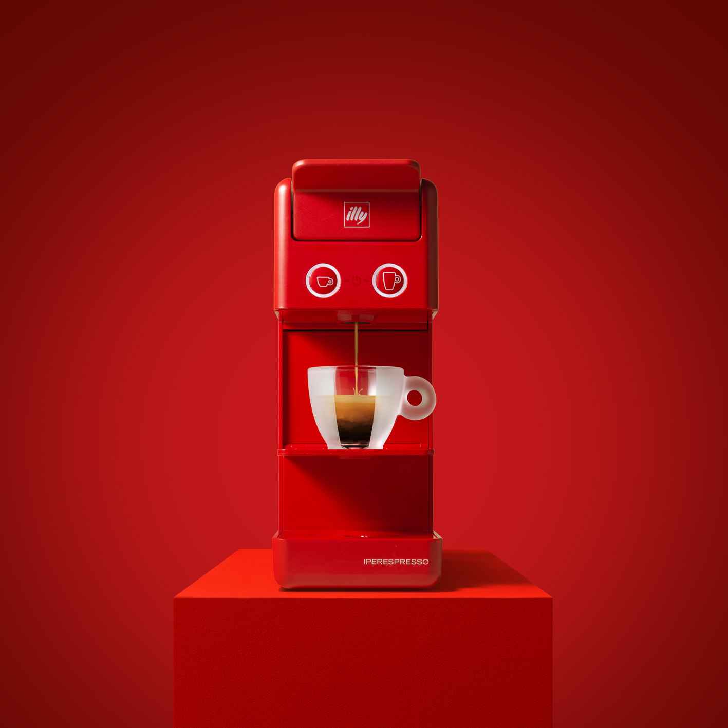 Macchina per espresso rossa che eroga caffè in una tazza di vetro su una superficie rossa.