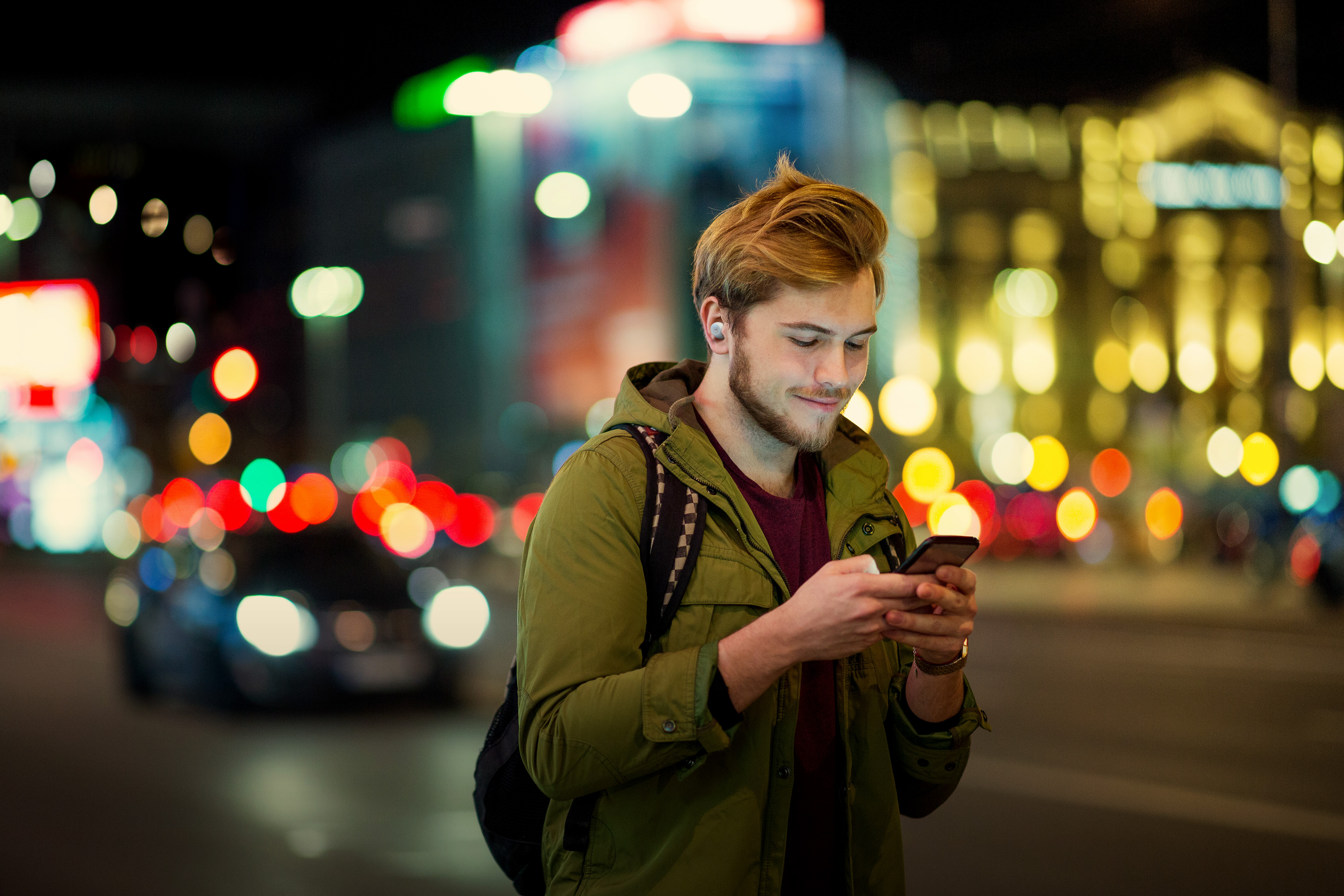 Un uomo usa un telefono per strada di notte. Lo sfondo mostra luci della città e auto.