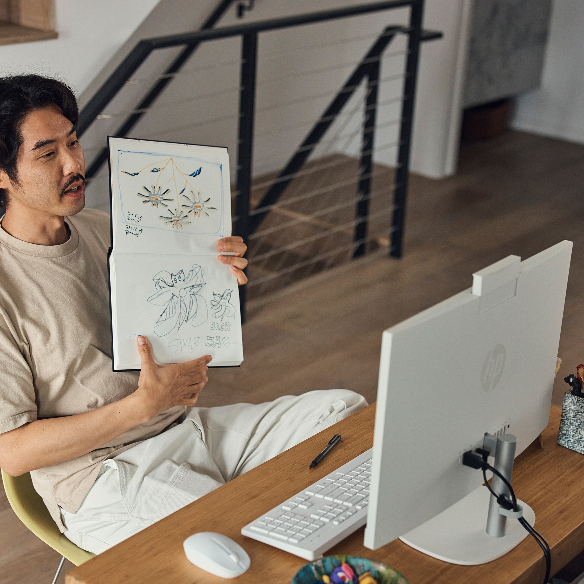 Mężczyzna trzyma notatnik, tłumacząc. Komputer, biurko i schody w tle.