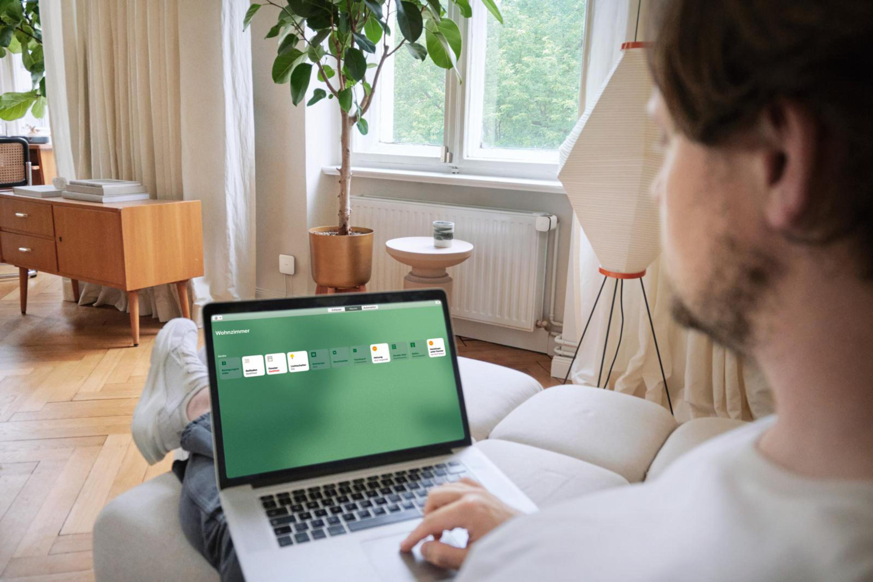 Ein Mann, der einen Laptop benutzt, sitzt auf einem Sofa in einem Wohnzimmer mit grünem Bildschirm.