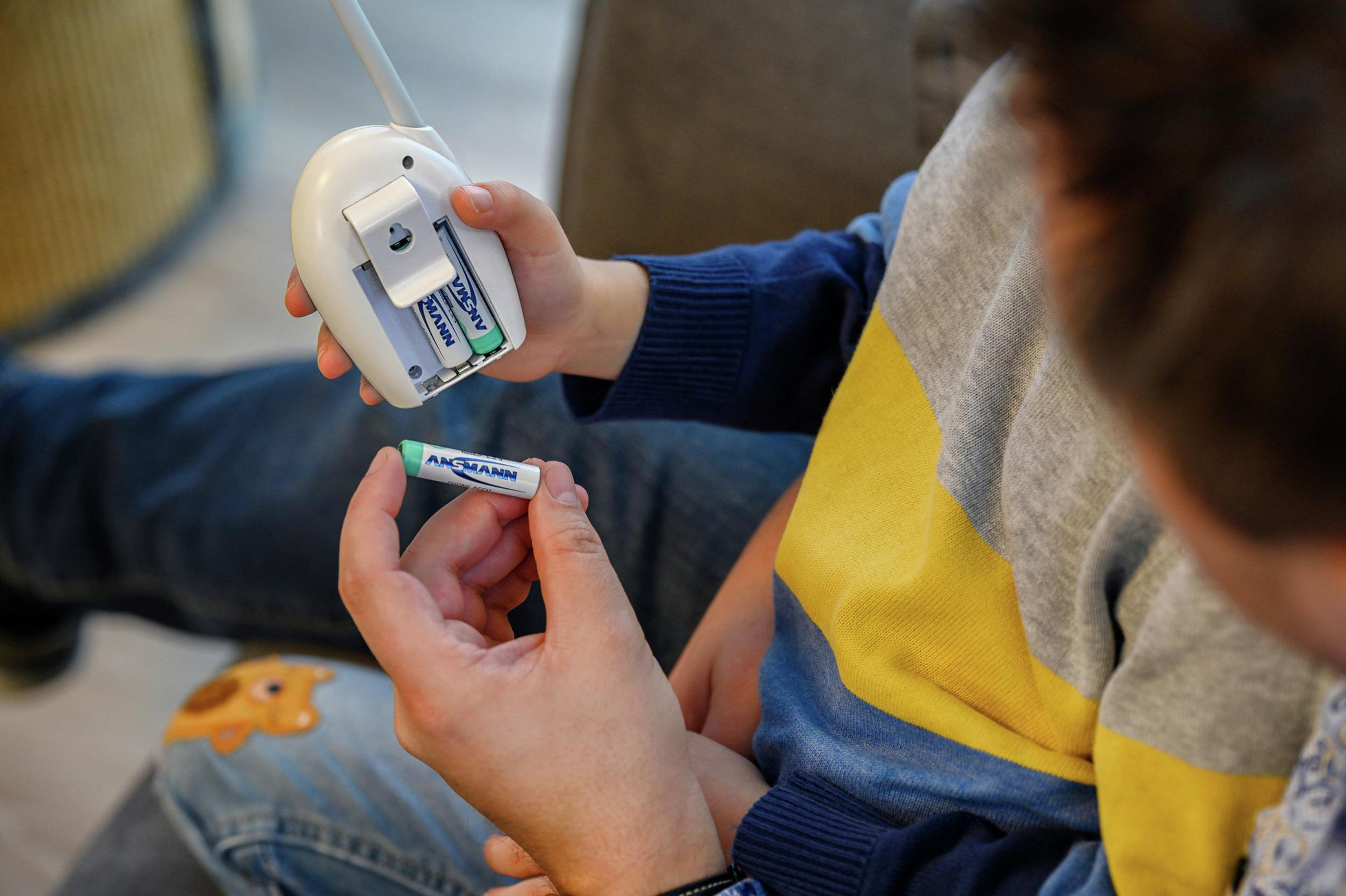 Dziecko trzymające baterię i nianię elektroniczną. Dorosły mu pomaga.