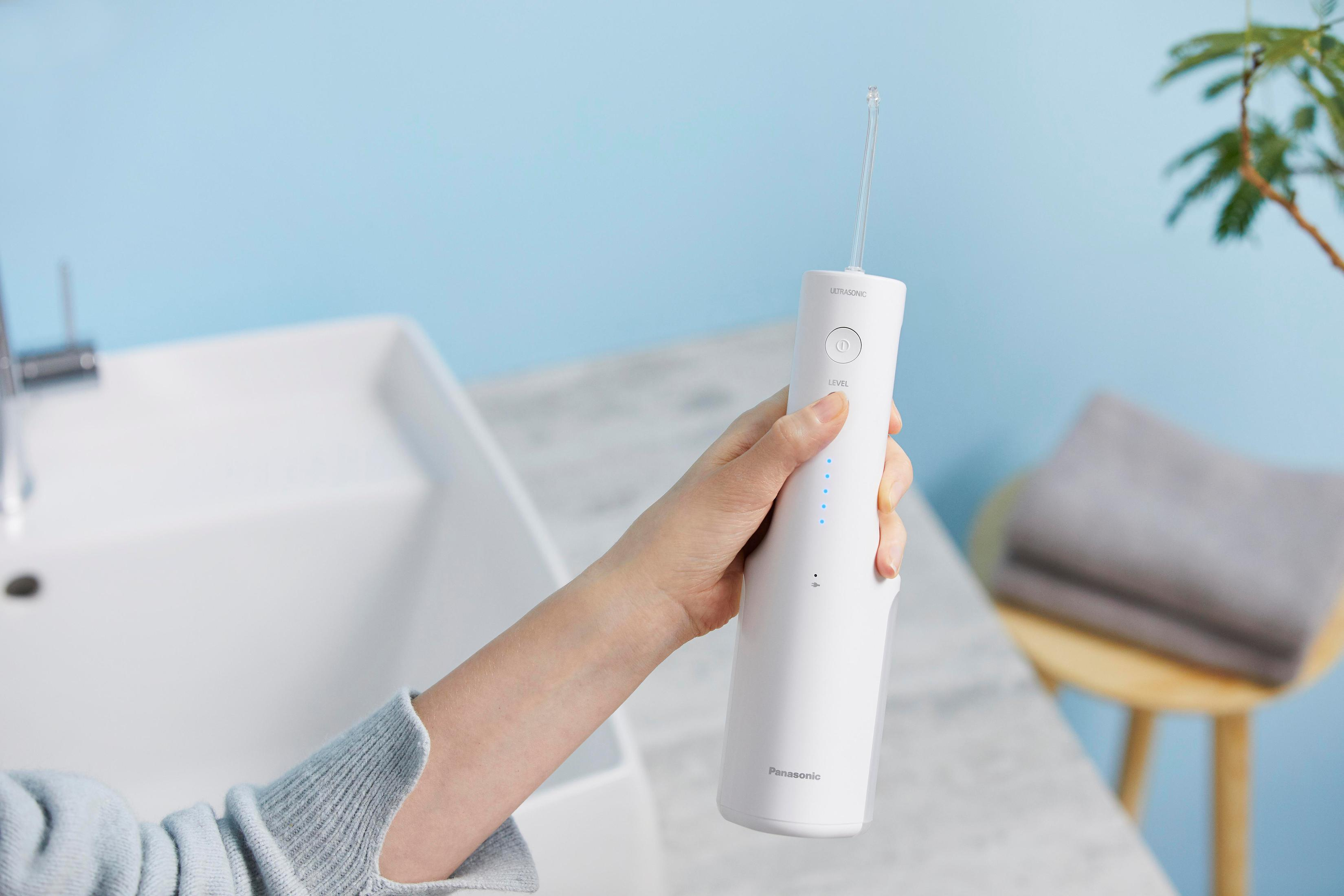 Die Hand einer Person, die einen weißen elektrischen Munddusche mit Wassertank hält.