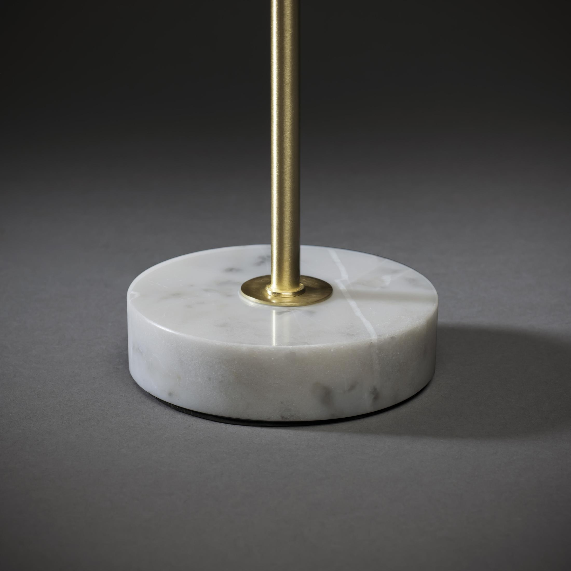 Weißer Marmor-Lampensockel mit einer goldenen Stange auf dunklem, grauem Hintergrund.