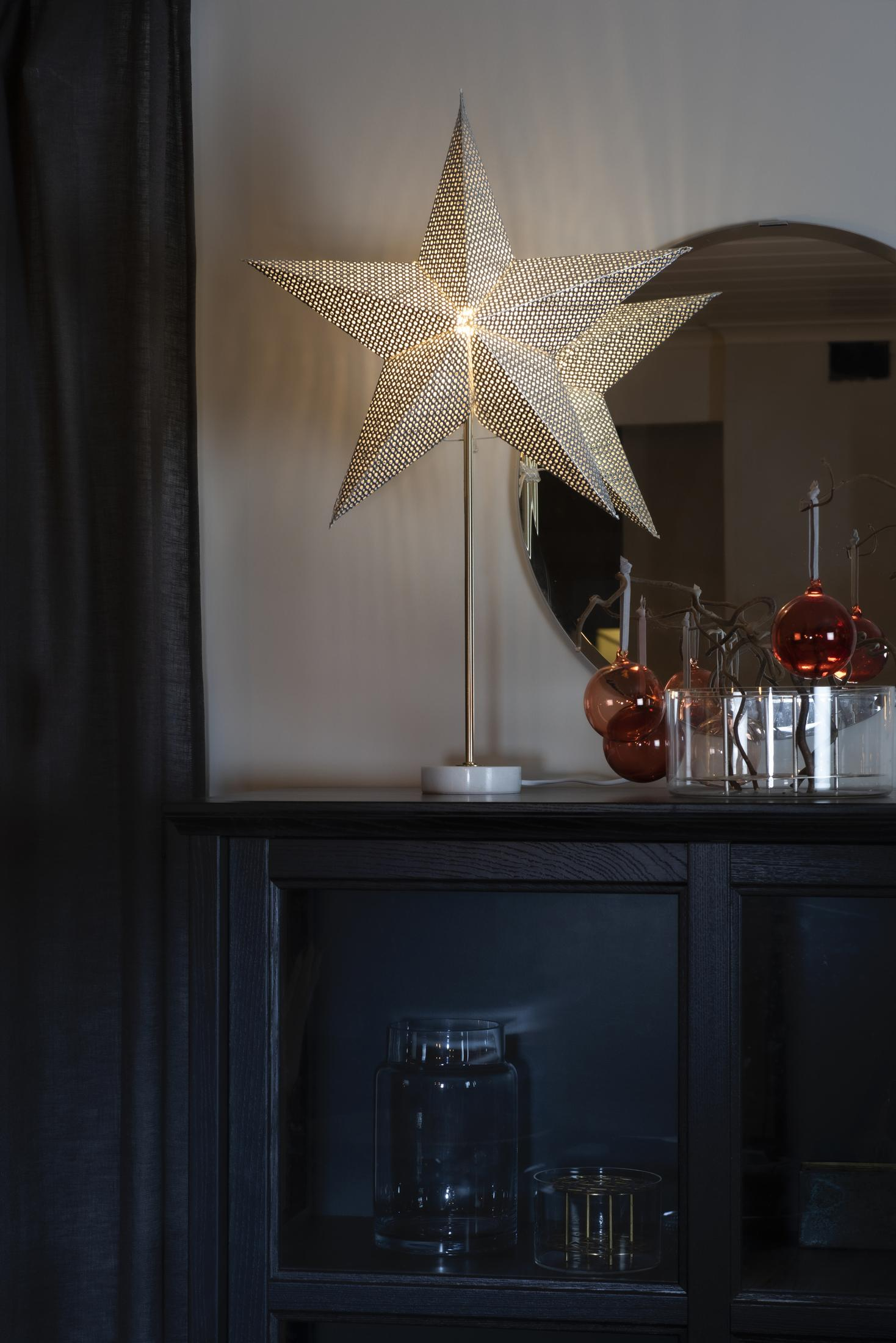 Sternförmige Leuchte auf dunklem Regal. Dahinter Spiegel und Weihnachtsschmuck.