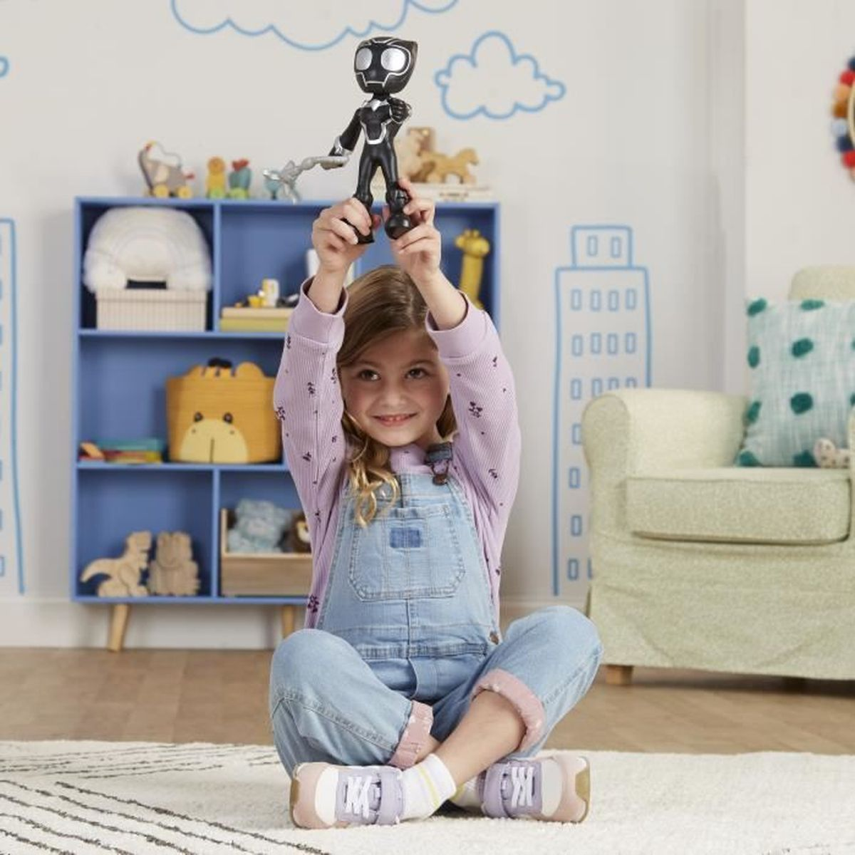 Młoda dziewczyna trzymająca zabawkę Black Panther wysoko nad głową, uśmiechnięta. Tło obejmuje półkę na książki.