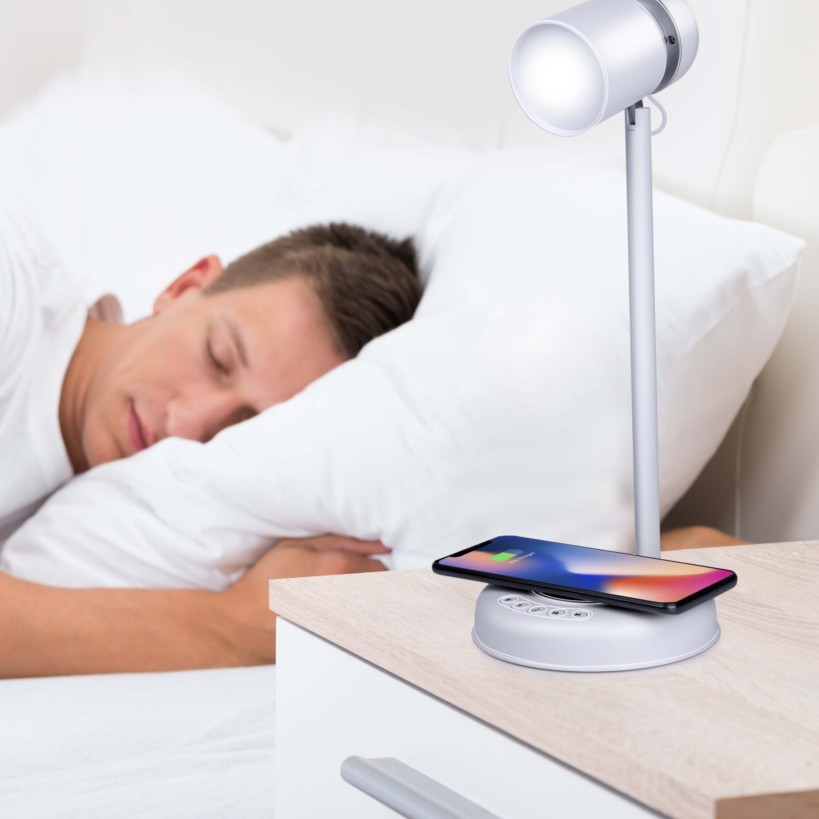 Homme dormant dans son lit, table de chevet avec lampe et téléphone en charge.
