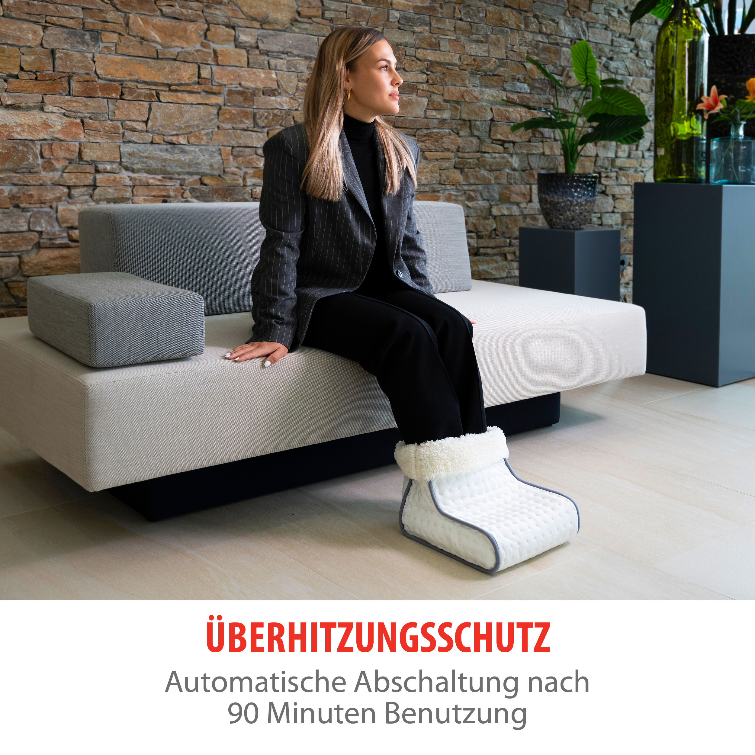 A woman sitting on a sofa wearing a foot warmer. Stone wall background with a text about overheating protection.