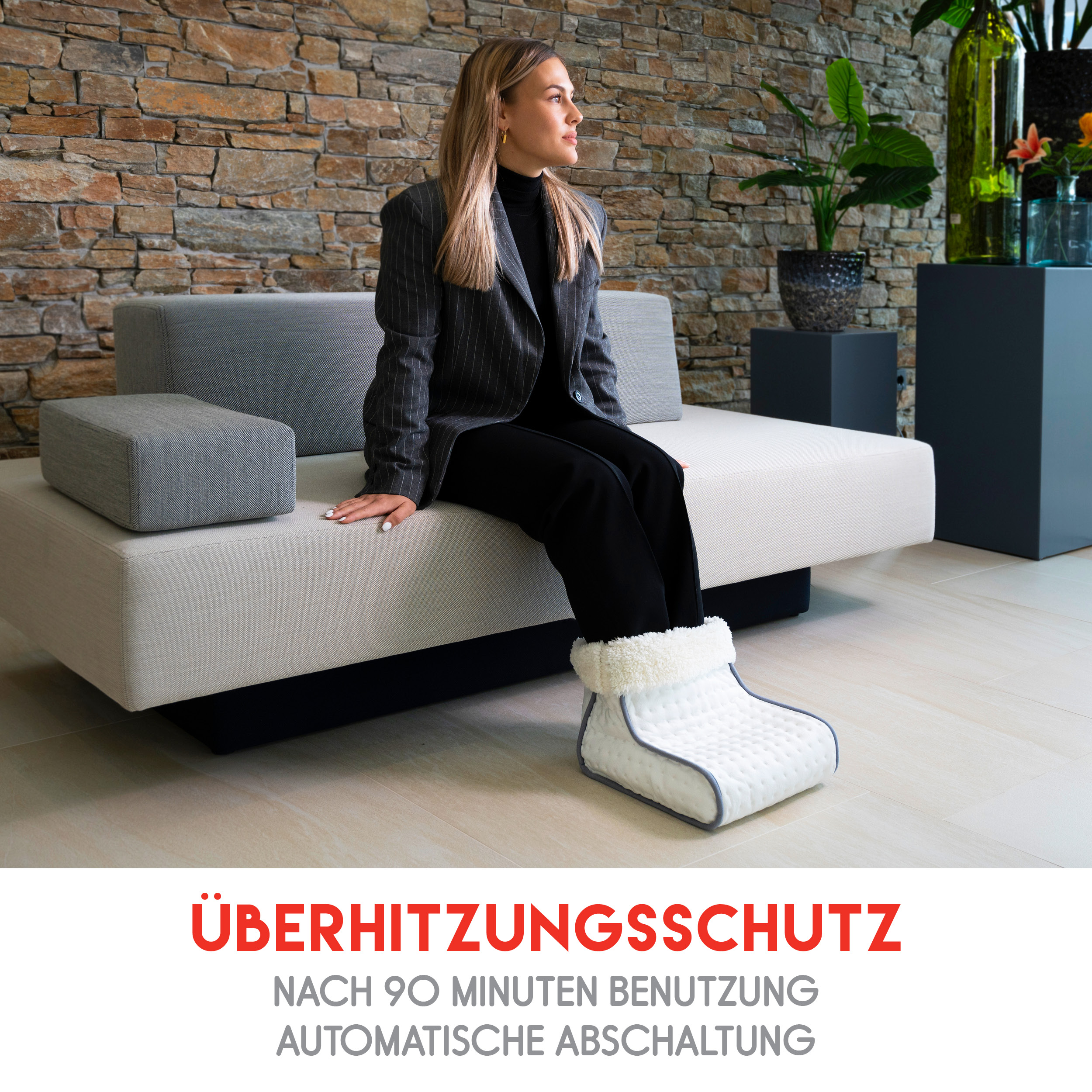 Woman wearing foot warmer, sitting on a couch in front of a stone wall.