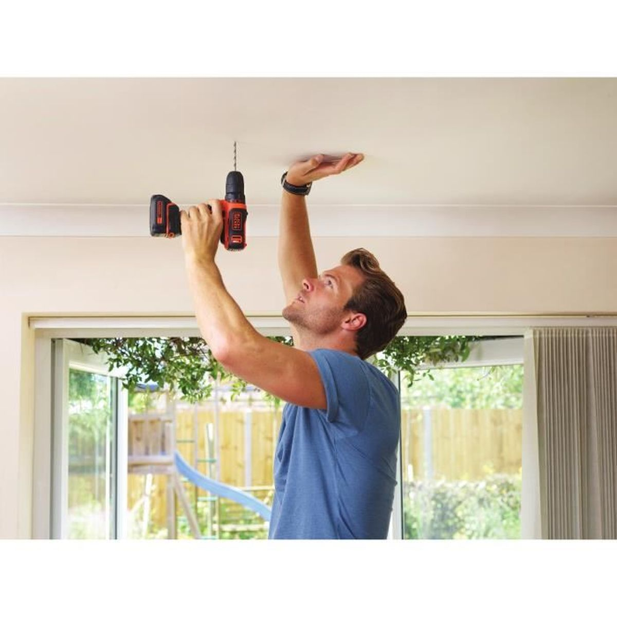 Mężczyzna wierci w suficie wiertarką w pokoju z oknem.