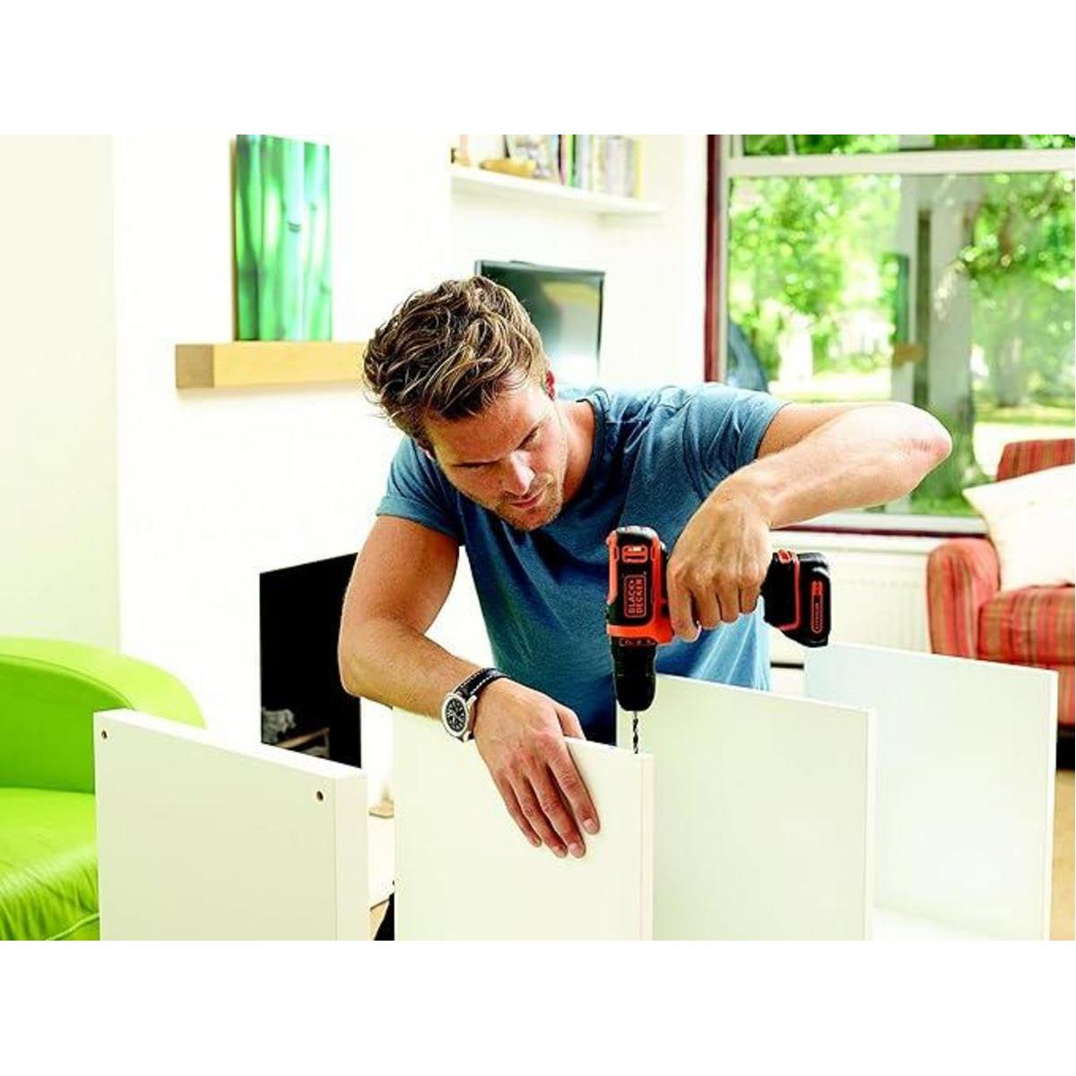 Mężczyzna używa wiertarki na białej szafce. Tło pokazuje pokój z oknem, kominkiem i zieloną sztuką ścienną.