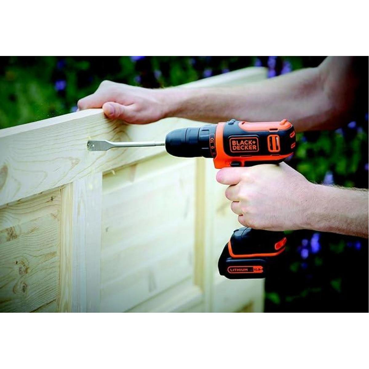 Osoba wierci w drewnianej konstrukcji czarno-pomarańczową wiertarką.