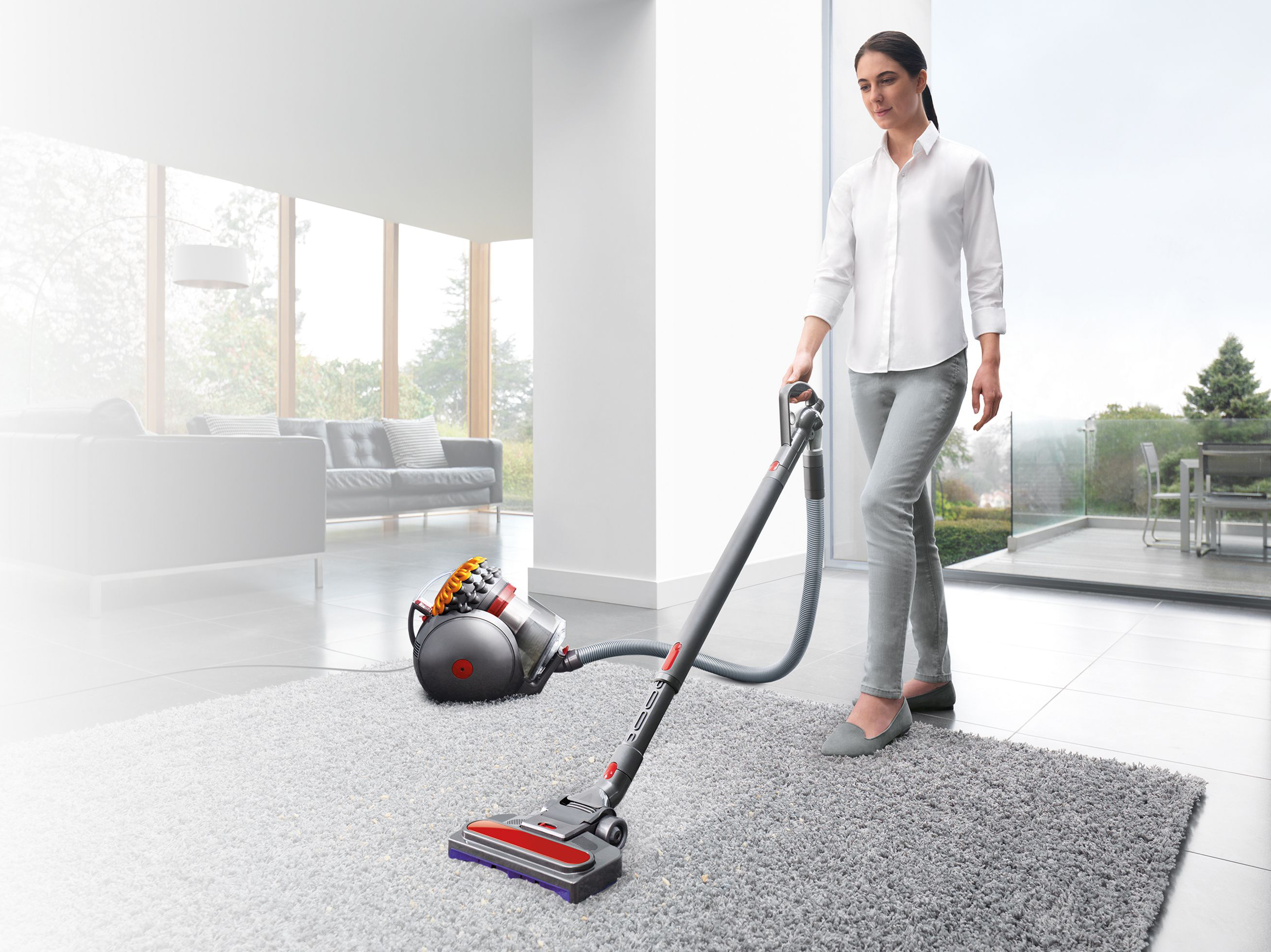 Donna che aspira un tappeto grigio con un aspirapolvere Dyson in una stanza luminosa e moderna.