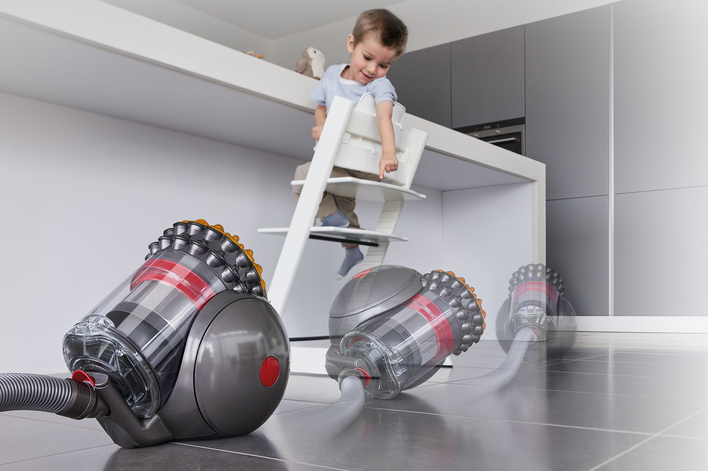 Un bambino su seggiolone osserva l'aspirapolvere che si muove sul pavimento.