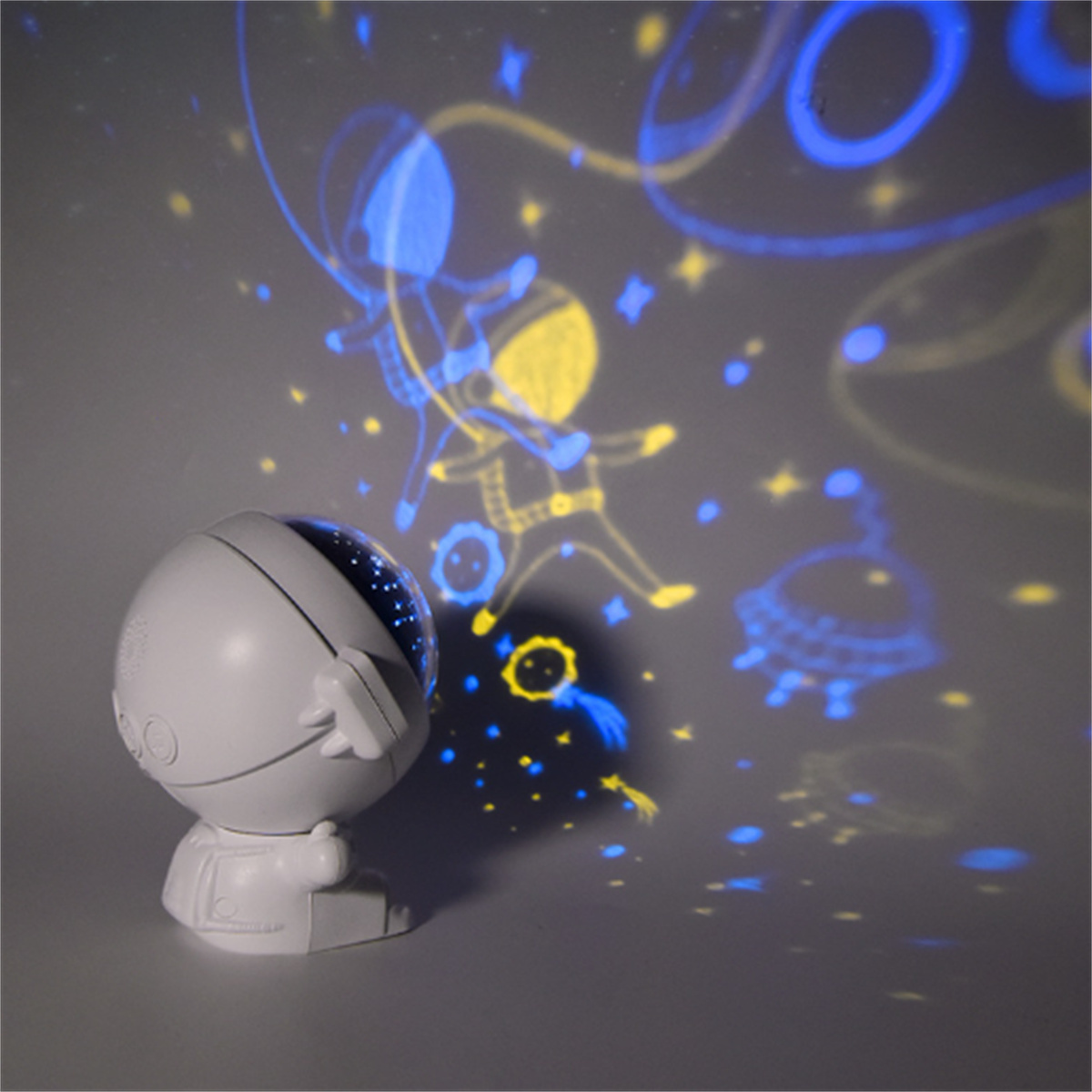 Ein weißer Projektor in Astronautenform, der einen Sternenhimmel und Astronauten projiziert.