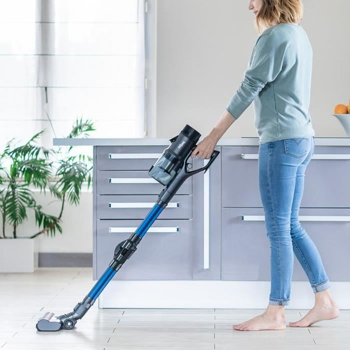Una donna che aspira il pavimento con un aspirapolvere senza fili in cucina.