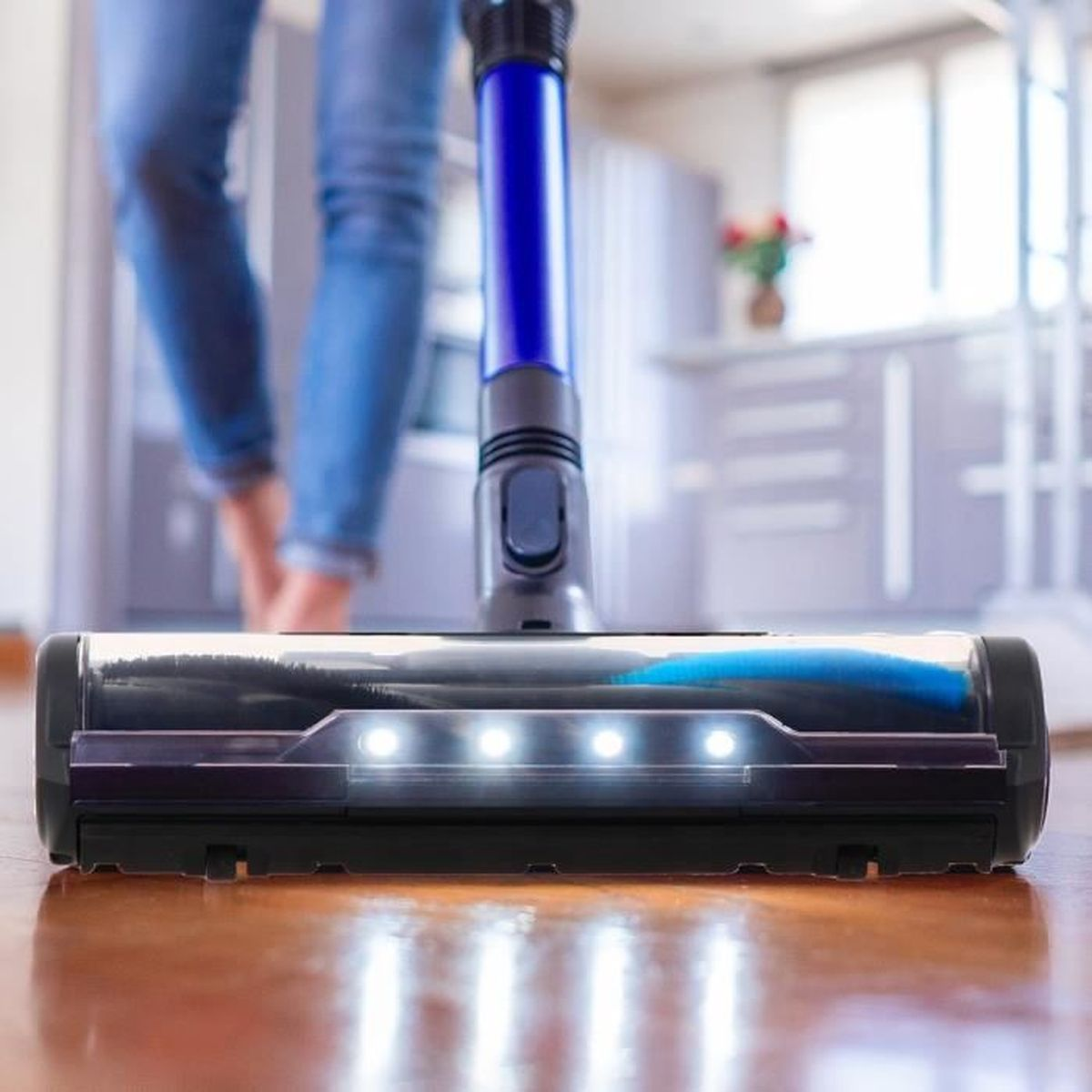 La parte anteriore di un aspirapolvere con le luci accese, che mostra il pavimento e le gambe di una persona.