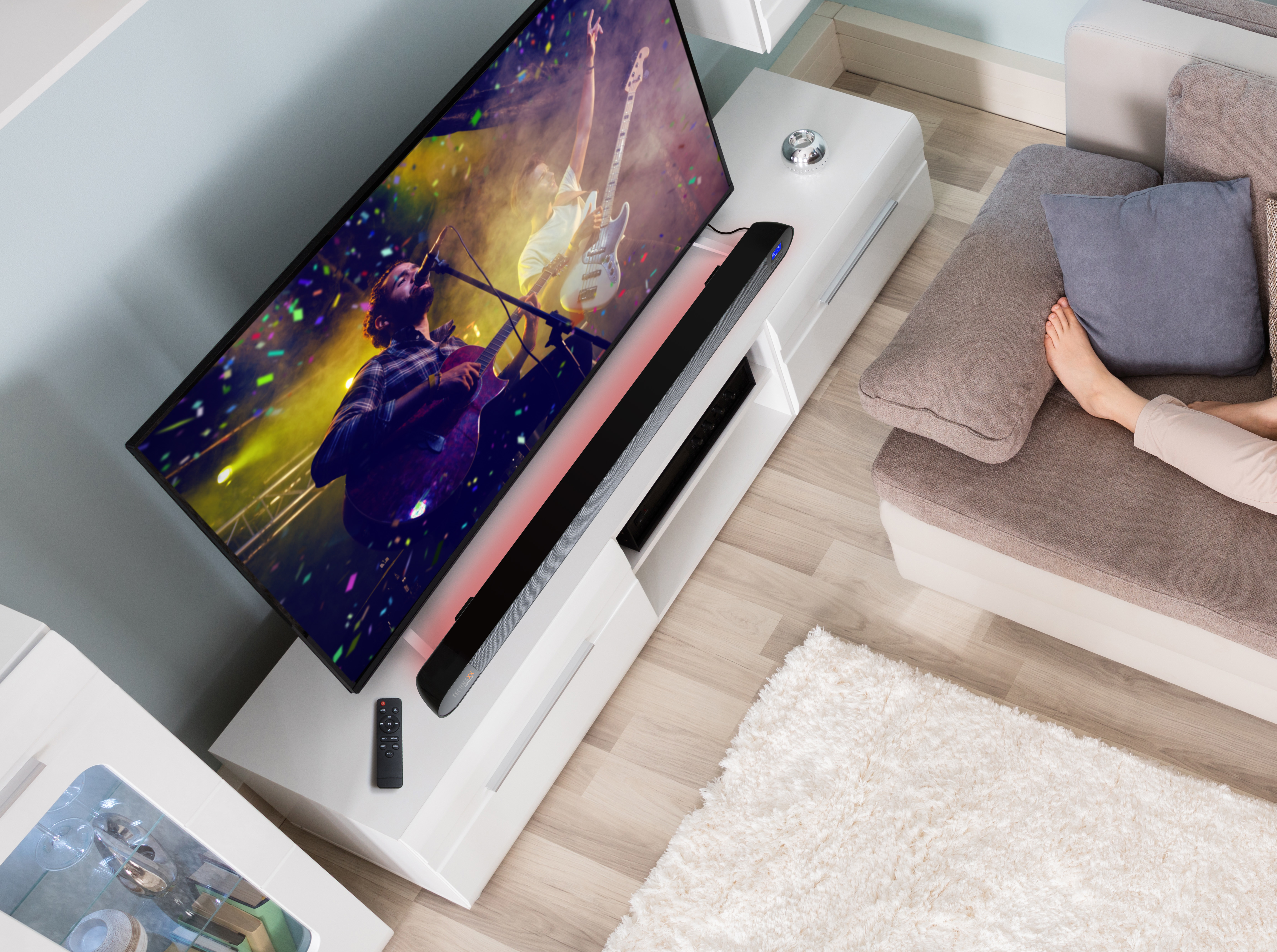 Soggiorno con TV, soundbar e piede di una persona. La TV mostra un concerto.